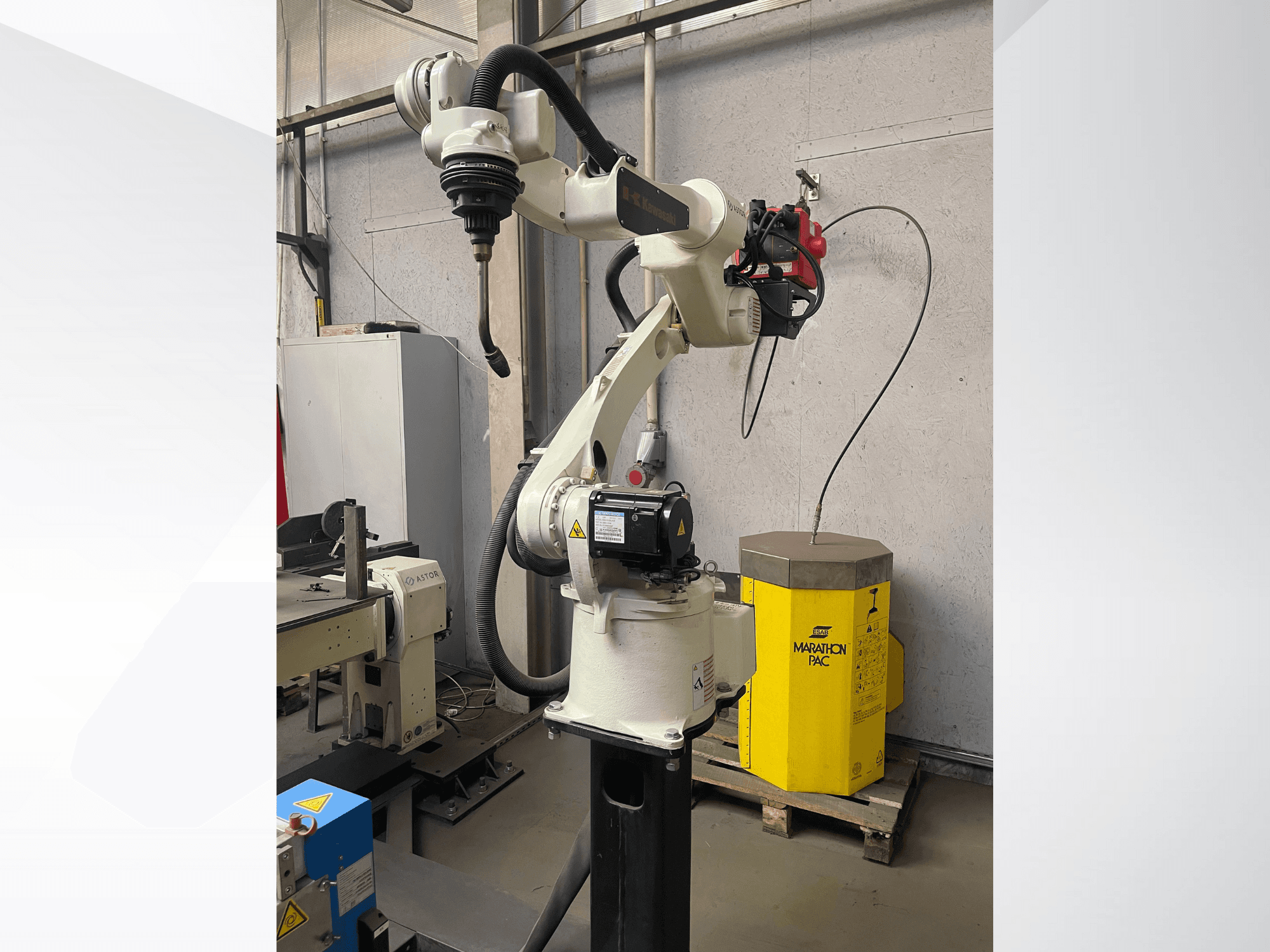 Kawasaki robotarm från sidan, med en monterad verktygshållare och en gul kraftenhet i bakgrunden.