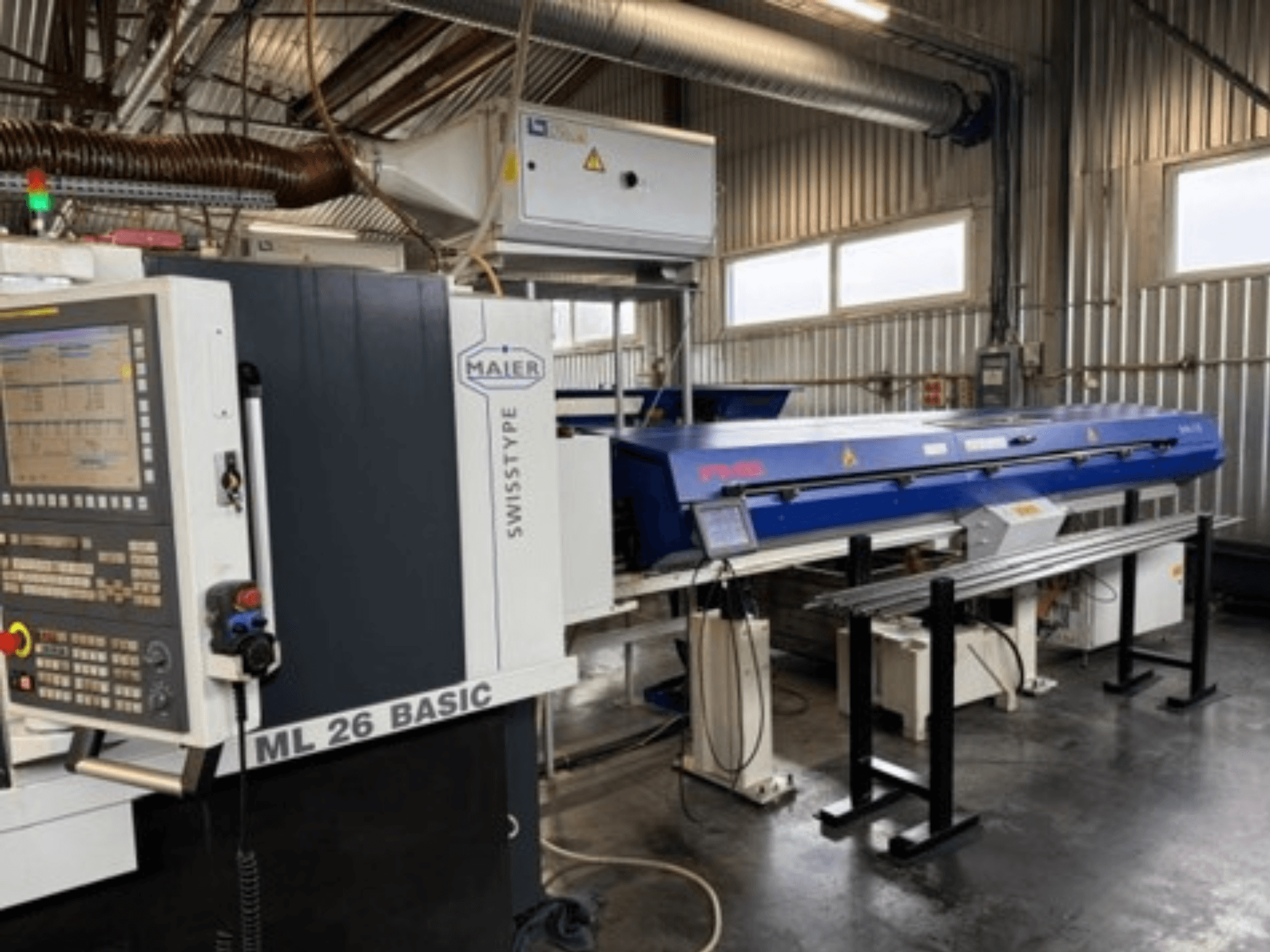 Alternativtext: Framifrånvy av en Maier ML26 C5Y Swiss Type-svarv med kontrollpanel och en blå enhet monterad på den, i en industriell miljö.