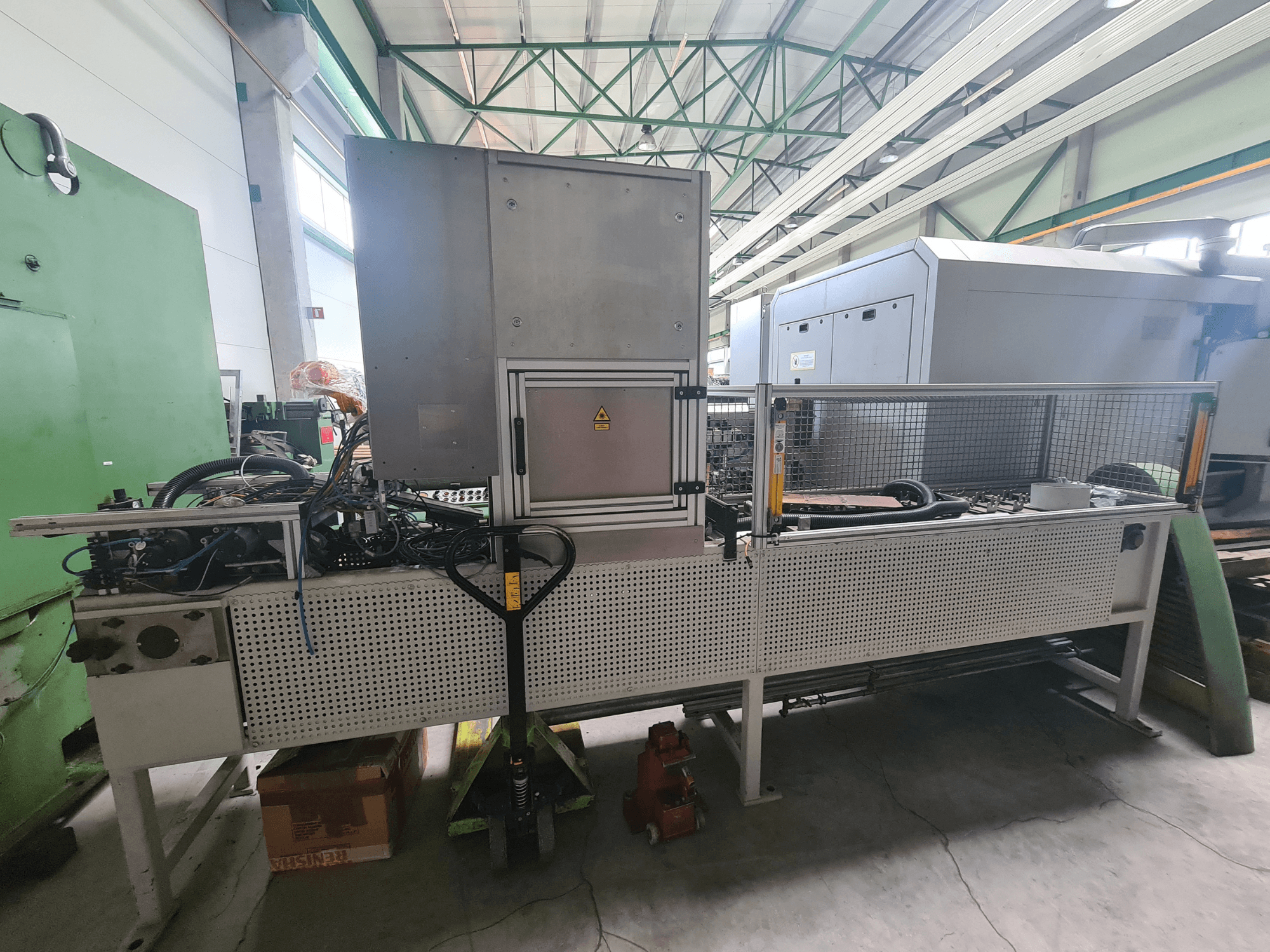 Industrimaskiner med metallram, slangar och kontrollpanel, sedda från sidan i en fabriksmiljö.