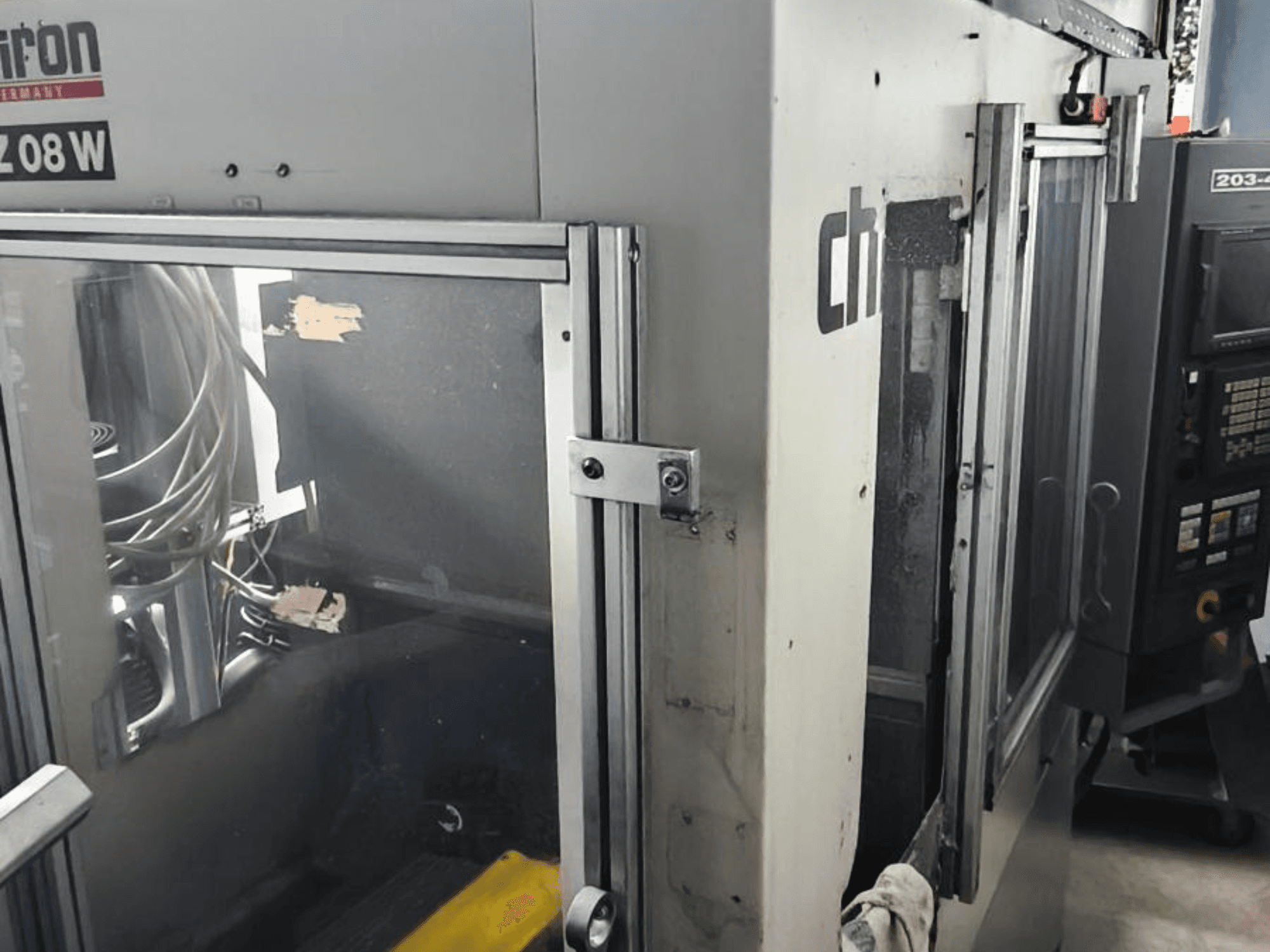 Vertikal bearbetningscenter CHIRON FZ 08 W, framifrån med kontrollpanel och delvis öppna dörrar, med synliga inre komponenter.