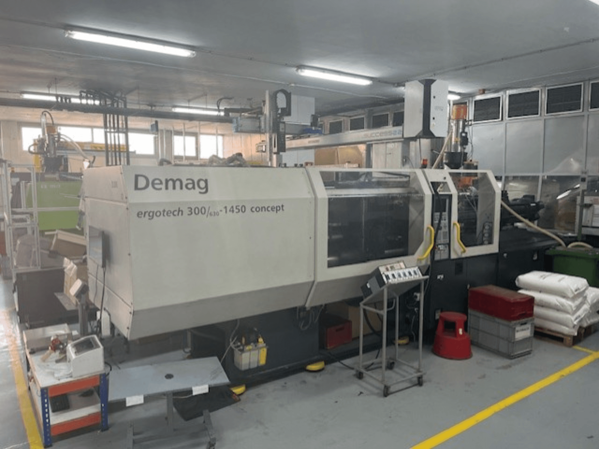 Demag ERGOTECH CONCEPT 3000-1450 hydraulisk formsprutningsmaskin, framifrån med manöverreglage och material i närheten.