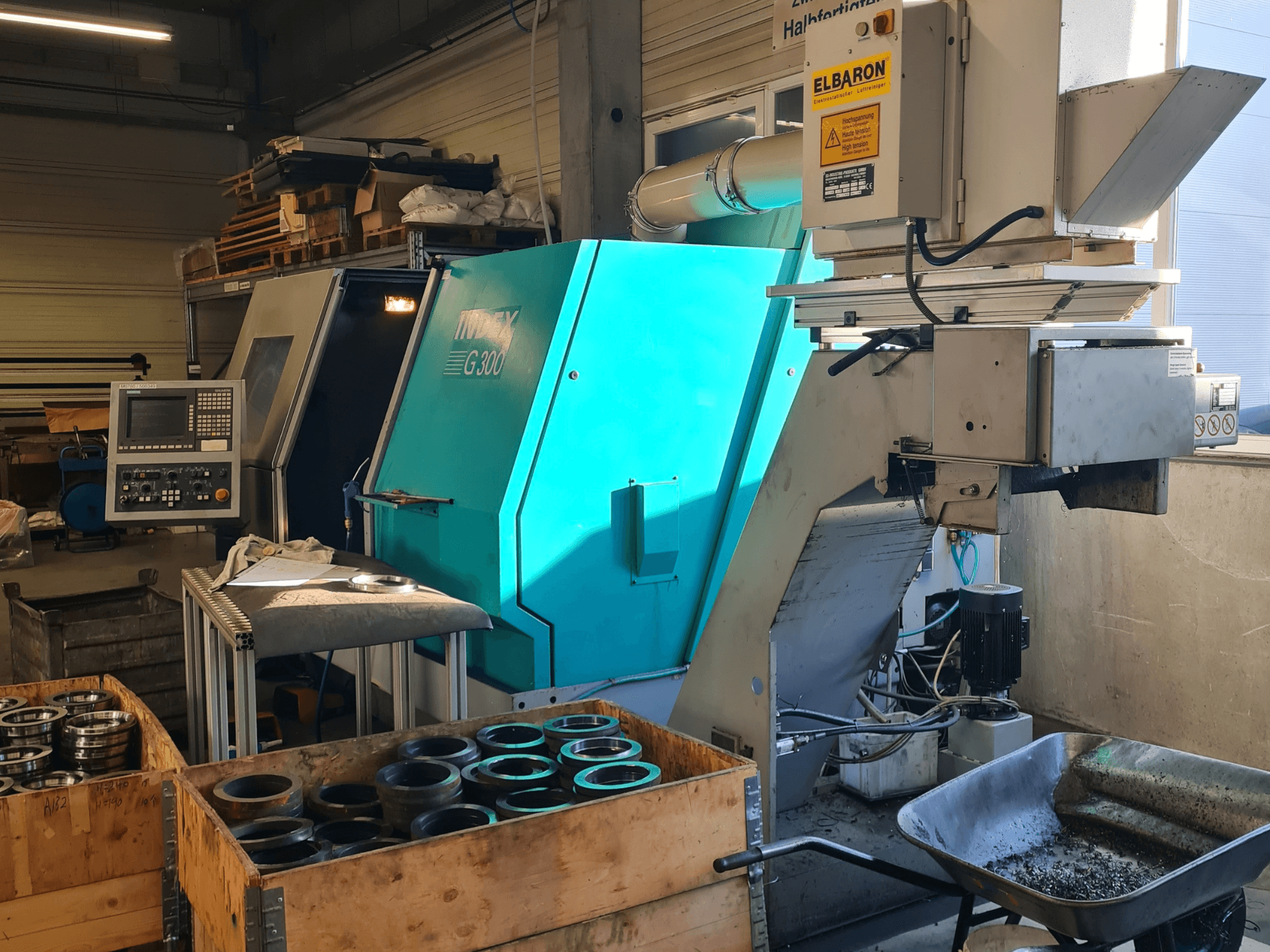 Framifrån sett: den horisontella svarven Index G300 RatioLine med manöverpanel, omgiven av detaljer och en transportör.