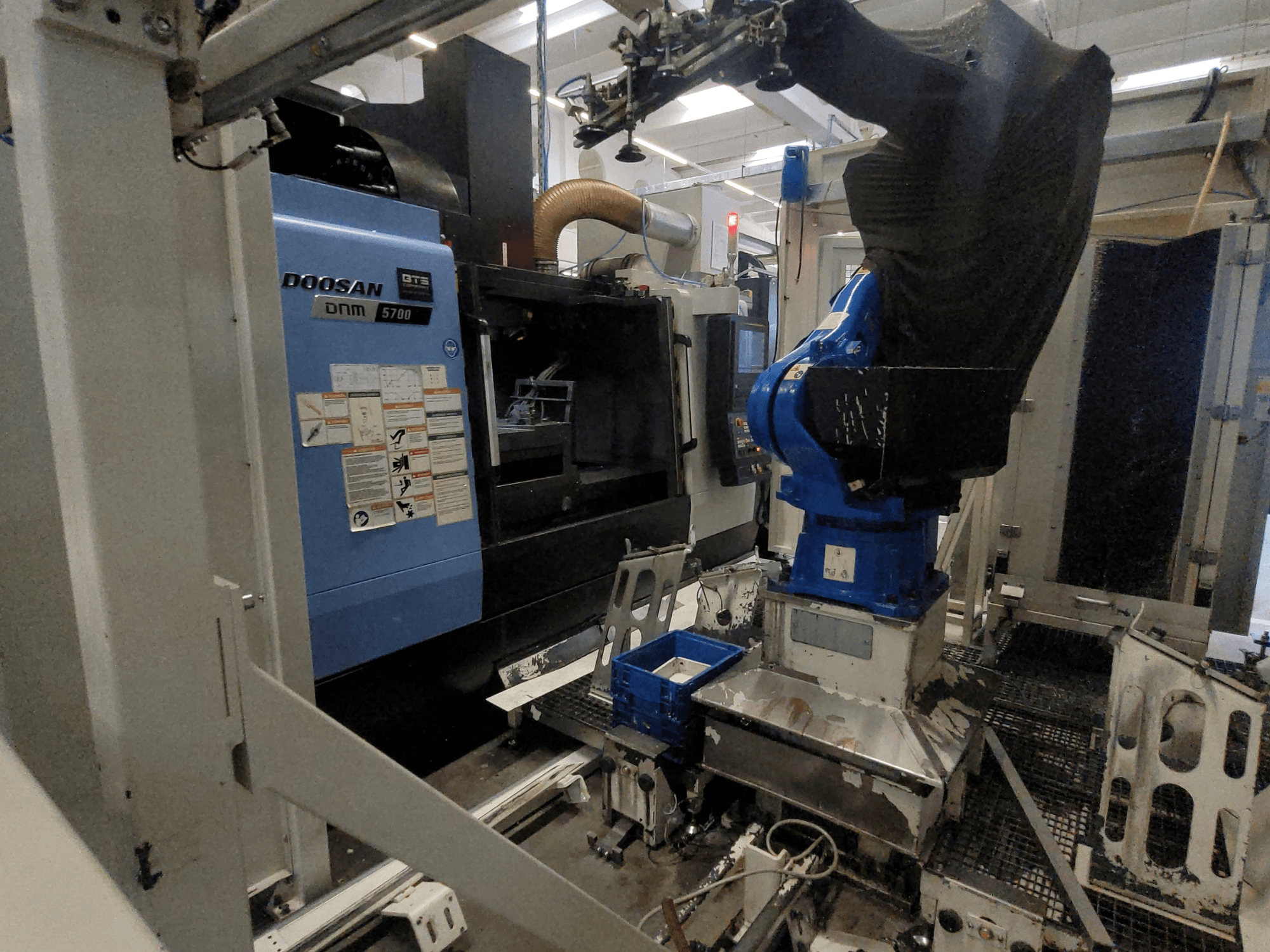 Ett vertikalt bearbetningscenter av typen DOOSAN DNM 5700 i en fabriksmiljö, där man ser en framifrånvy och hur robotarmen är integrerad.
