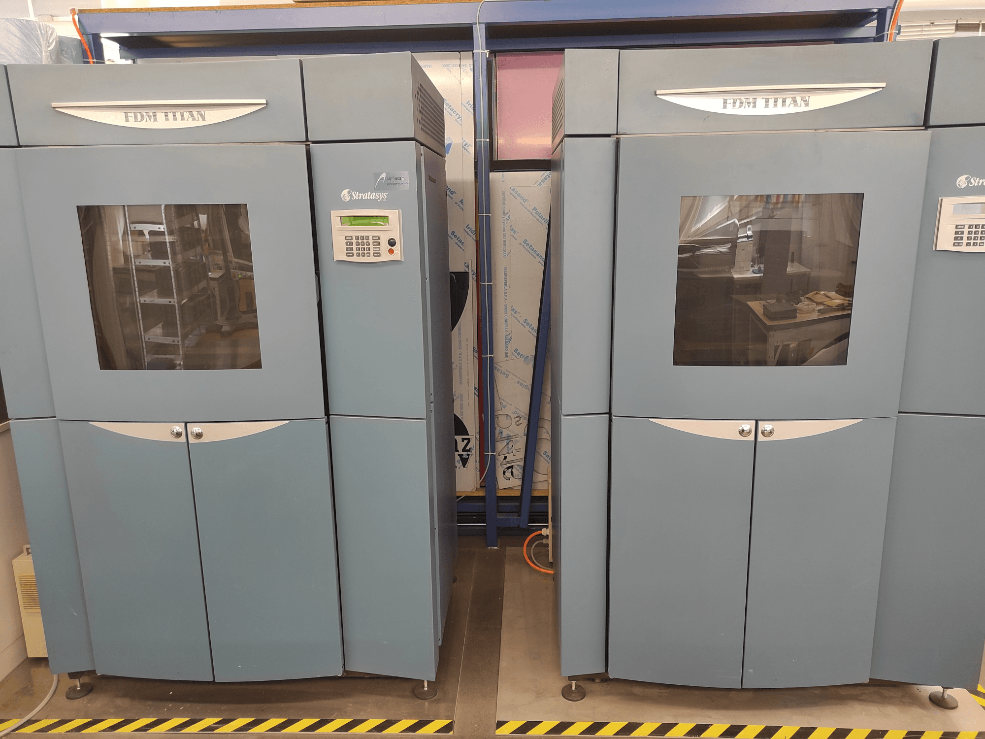 3D-skrivaren FDM TitanTI från Stratasys, sett framifrån, med dubbla luckor och kontrollpanel, placerad i en industriell miljö.