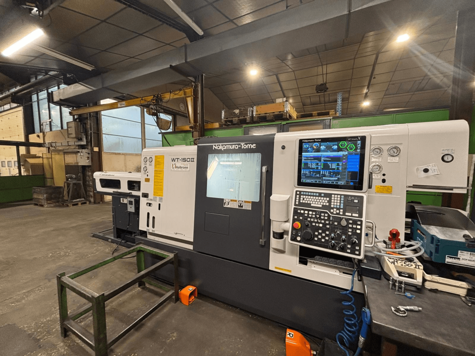 Nakamura-Tome WT-150II-maskin, framifrån, med kontrollpanel och verktyg synliga på en arbetsbänk i en verkstadsmiljö.