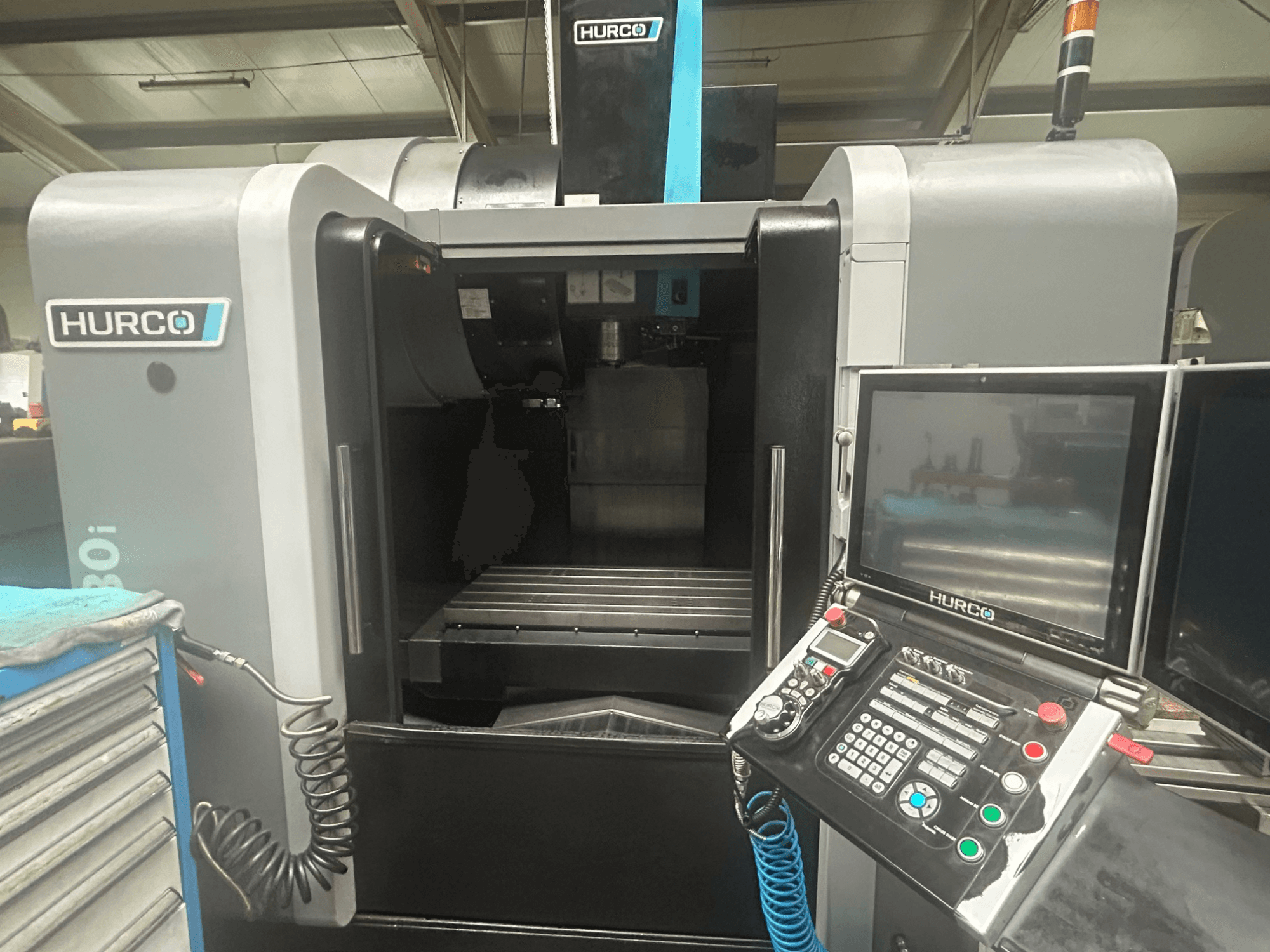 Hurco VM30i CNC-maskin framifrån, med kontrollpanel med knappar, display och förvaringsutrymme för verktyg.