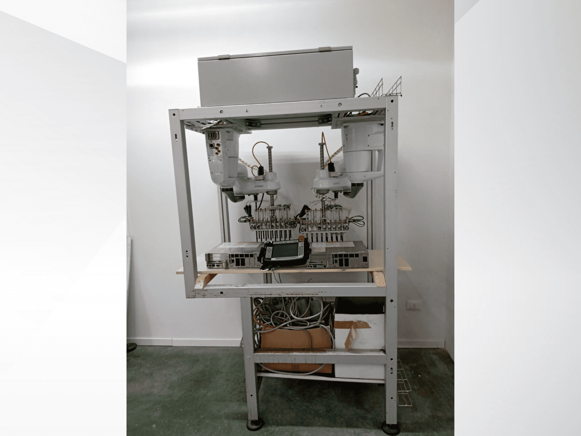 Automatiserad robotarbetsstation med dubbla armar, displayenhet och elektronik på en metallram, framifrån, avancerad teknikinstallation.