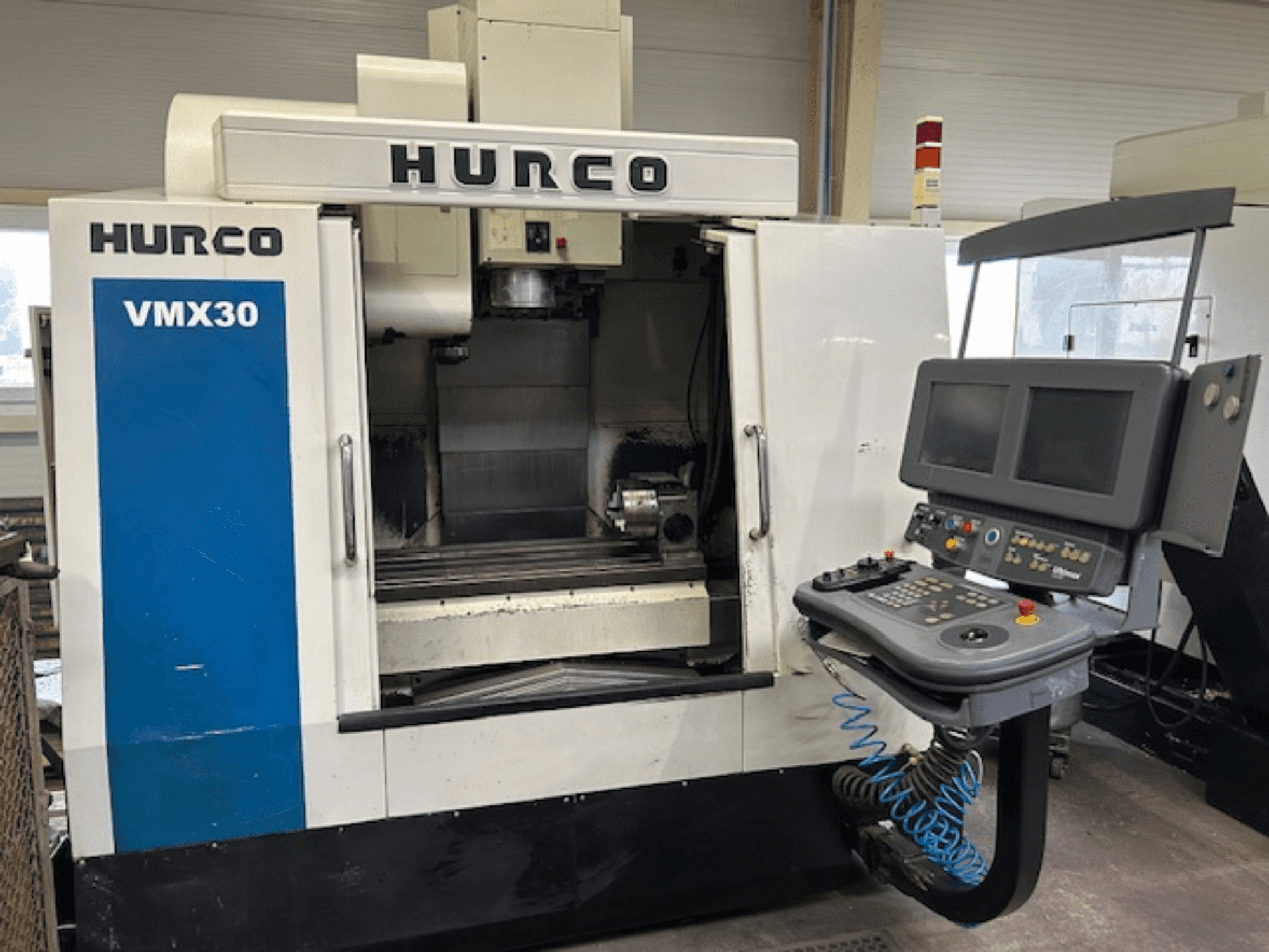 Hurco VMX30 CNC-fräsmaskin i en verkstad, vy framifrån; har kontrollpanel med dubbla skärmar och manöverknappar.