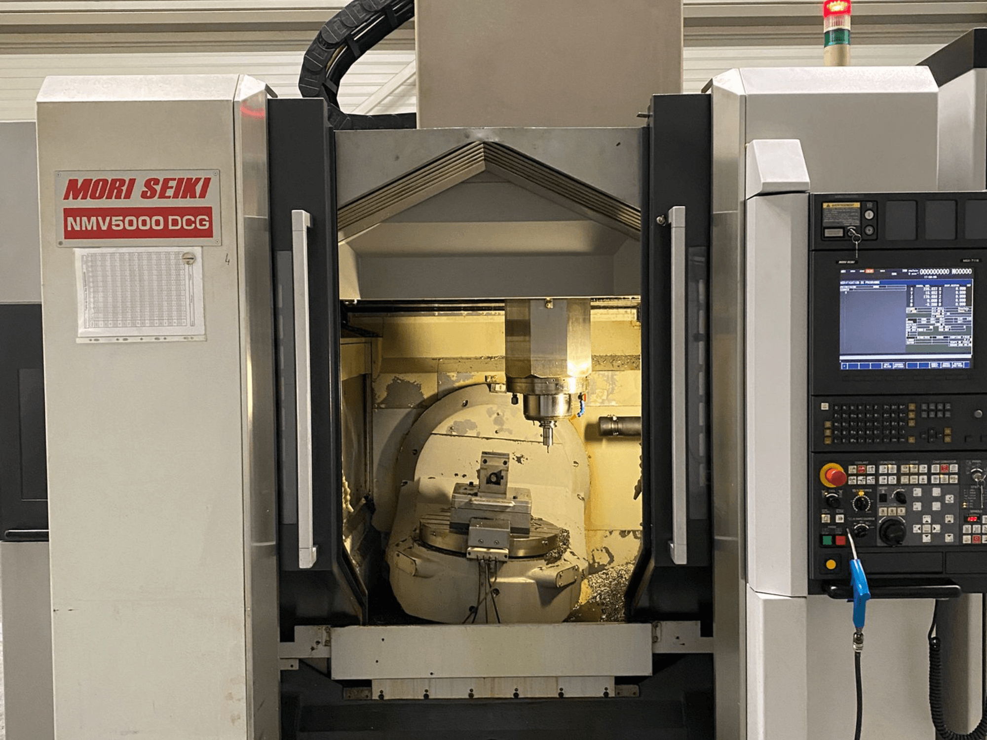 MORI SEIKI NMV 5000DCG universellt bearbetningscenter, framifrån med kontrollpanel och invändigt bearbetningsområde.