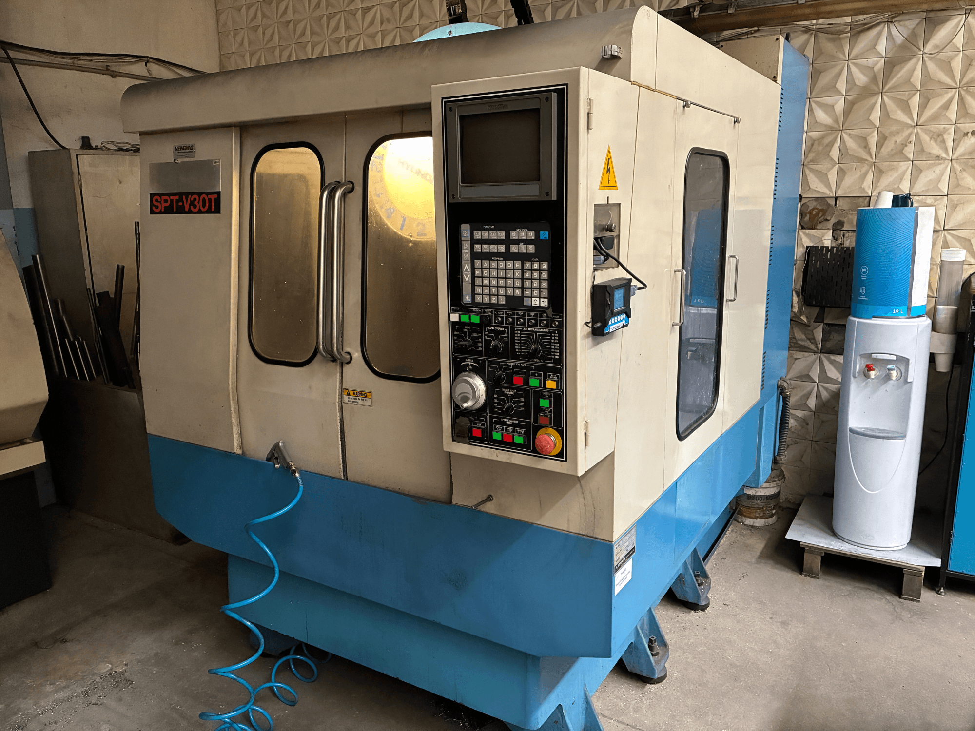 SPT-V30T CNC-maskin i blått och vitt, framifrån med kontrollpanel, dörrar och luftslang. Perfekt för precisionsbearbetning.