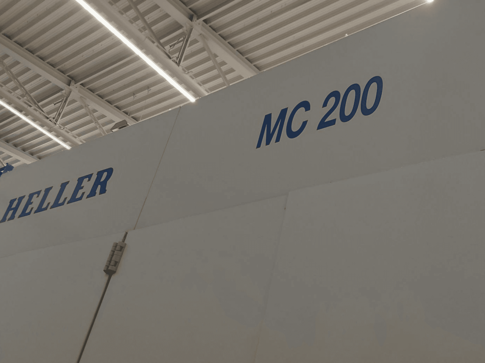 Heller MC 200 horisontell fleroperationsmaskin, sedd från sidan, med märke och modell i blå bokstäver på en vit yta.