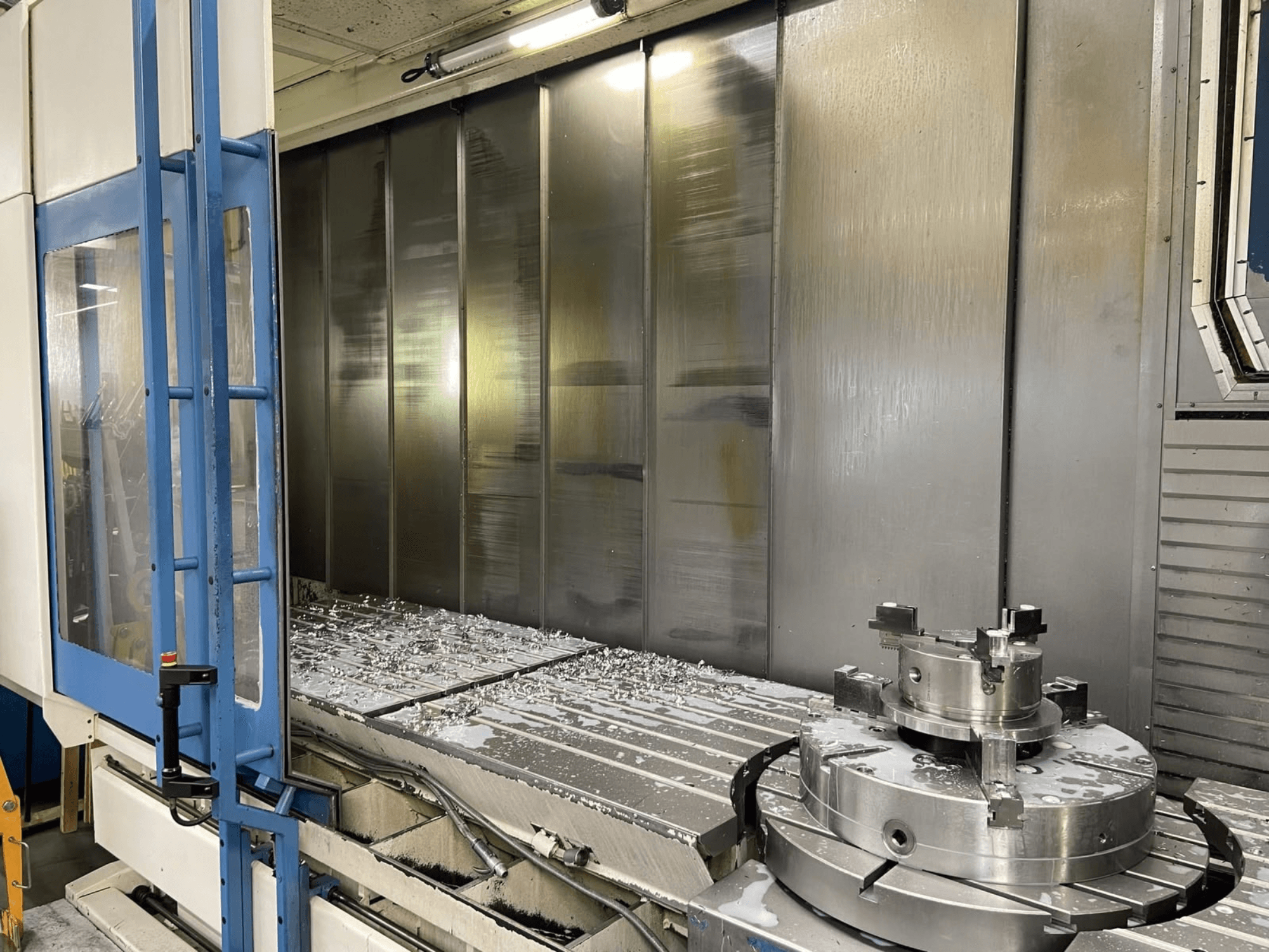AXA VHC-3-3000-M/E vertikalt bearbetningscenter, framifrån, där man ser frästa metallspån på arbetsbordet och skärverktygen.