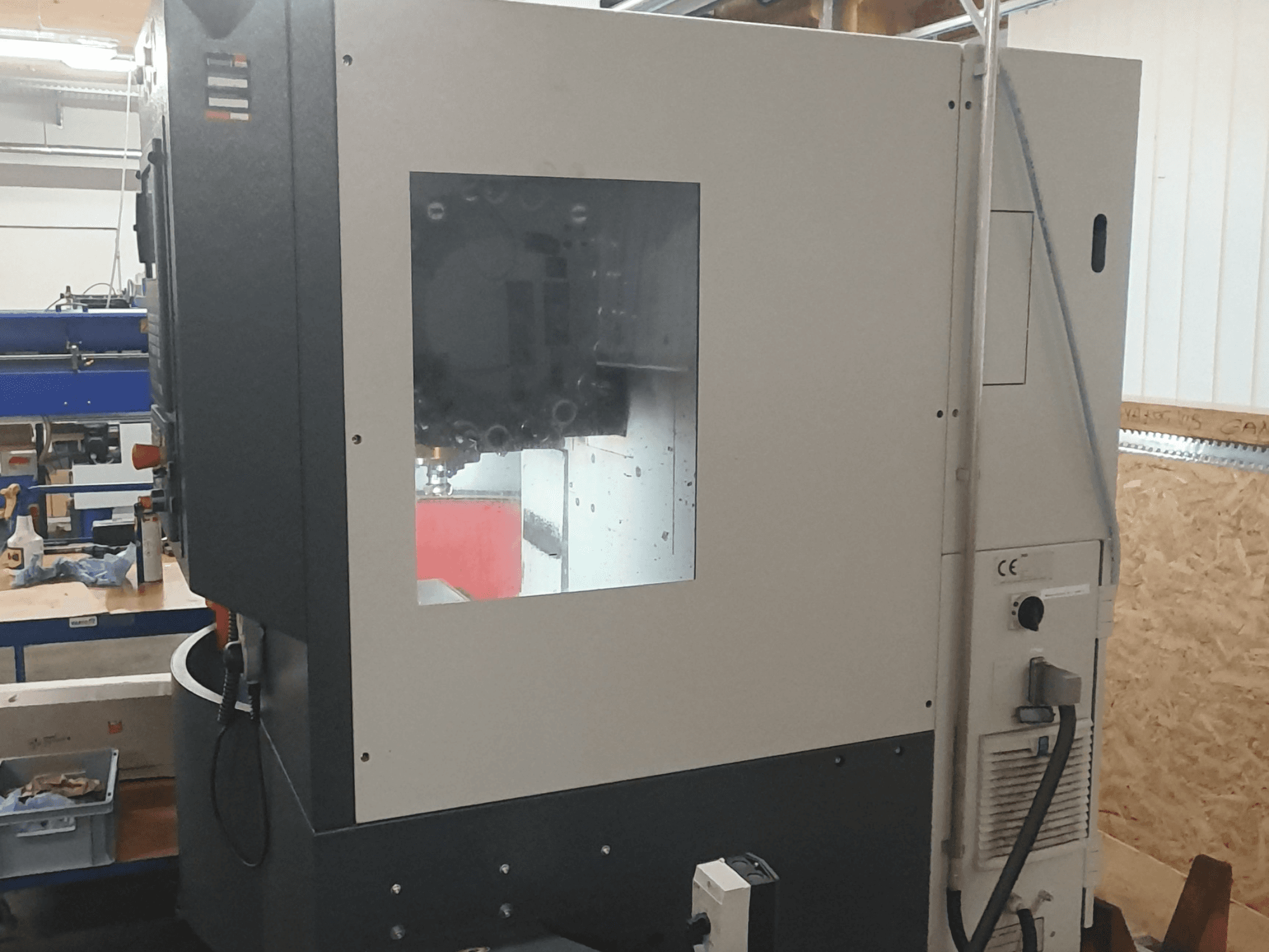 Sidovy av en metallbearbetningsmaskin med synlig kontrollpanel, stort visningsfönster och invecklade inre komponenter.