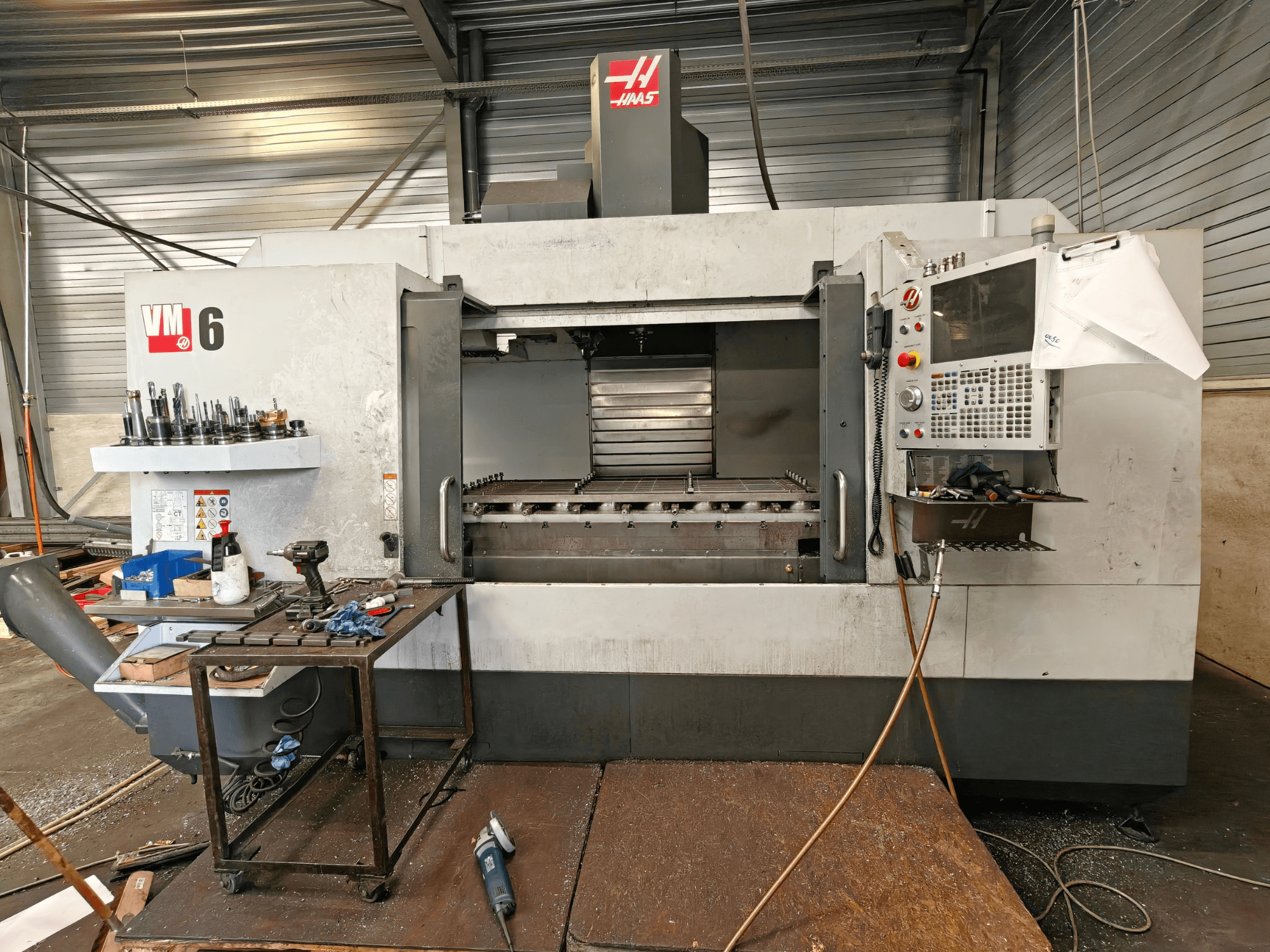 Haas VM-6 vertikalt bearbetningscenter, framifrån sett, med verktygsförvaring, kontrollpanel och synliga spån i arbetsområdet.