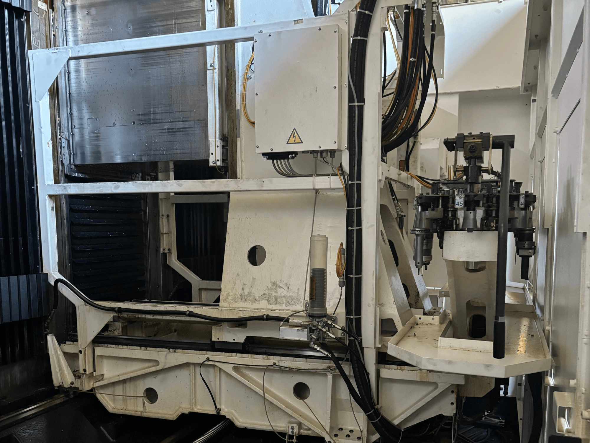 Industriell maskin i sidovy som visar en vit CNC-fräsmaskin med synliga verktyg, rör och kontrollpanel.