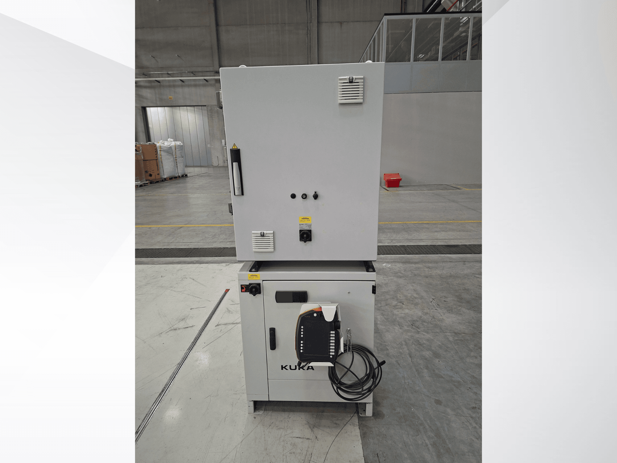 KUKA KR 90 R2700 PRO C4 FLR-robotarmstyrenhet, framifrån sett med kontrollpanelen och säkerhetsetiketterna i ett rymligt lager.