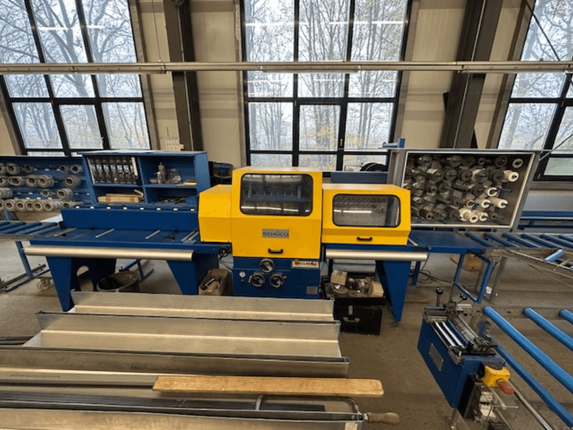 Frontvy av SCHÜCO ISOMAT 4 verktygsmaskin med gul kontrollpanel, flera rullar och ett förvaringsfack.