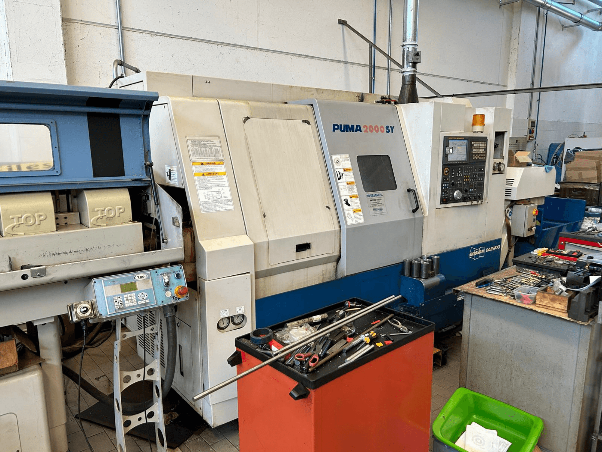 En horisontell svarv av typen DOOSAN PUMA 2000SY i en verkstad, sett från sidan med kontrollpanelen och verktygen i närheten.
