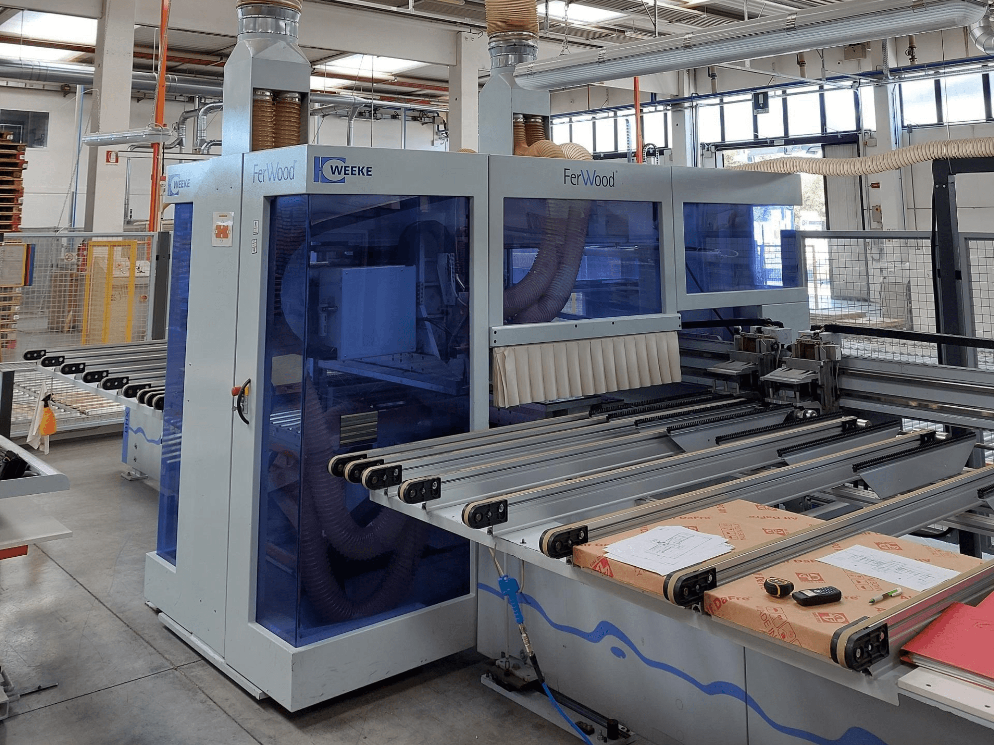 Weeke FerWood CNC-maskin i en verkstad, framifrån med blåtonade paneler, manöverknappar och arbetsbord med material.