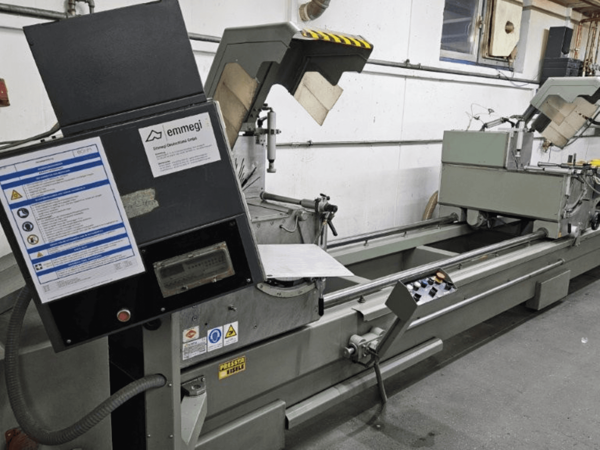 Emmegi industriell skärmaskin, framifrån, med kontrollpanel, säkerhetsetiketter och operativa komponenter.