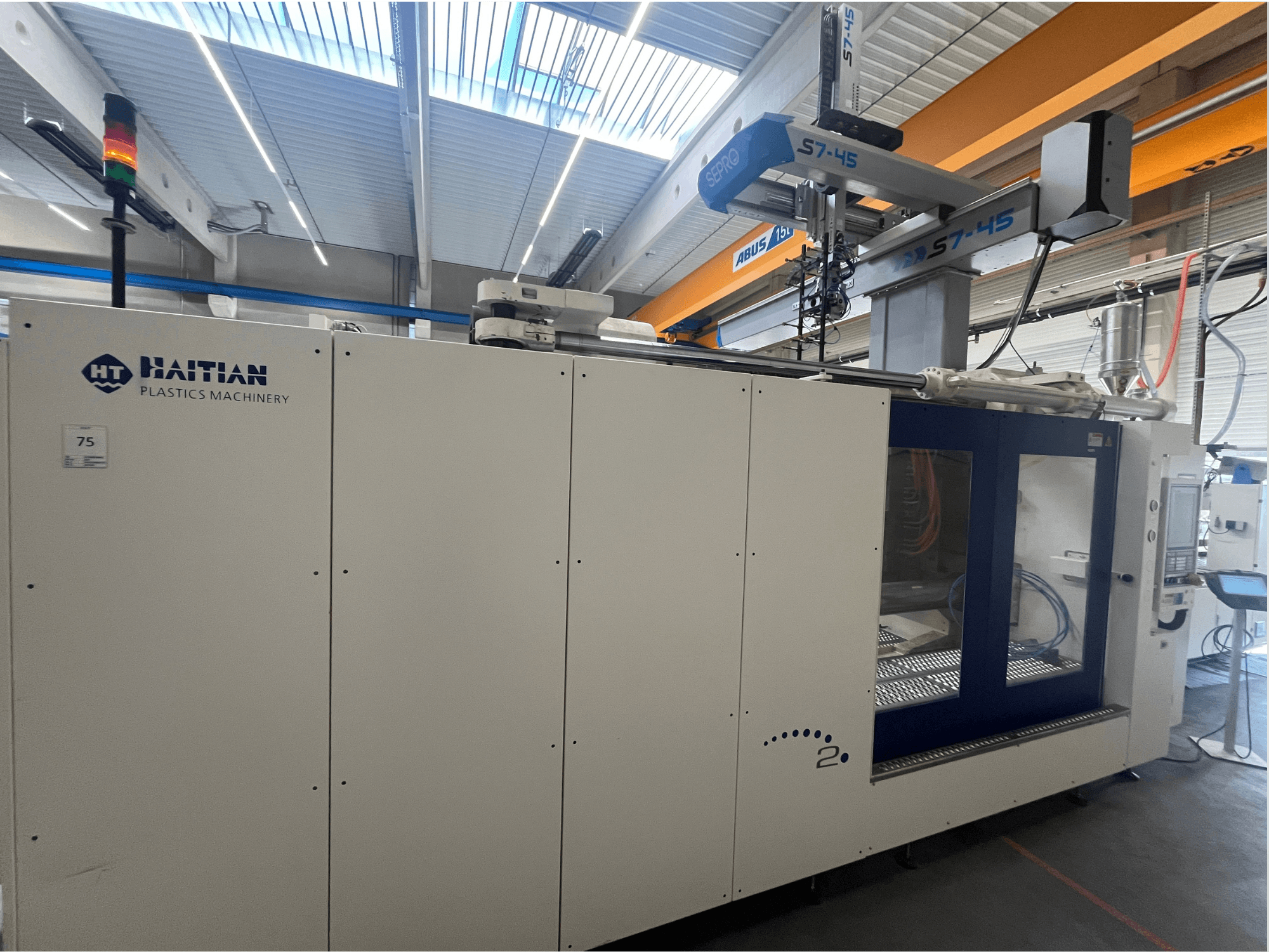 Haitisk S7-45 formsprutningsmaskin i sidovy med kontrollpanel och säkerhetsljusindikator. Vit och blå design.