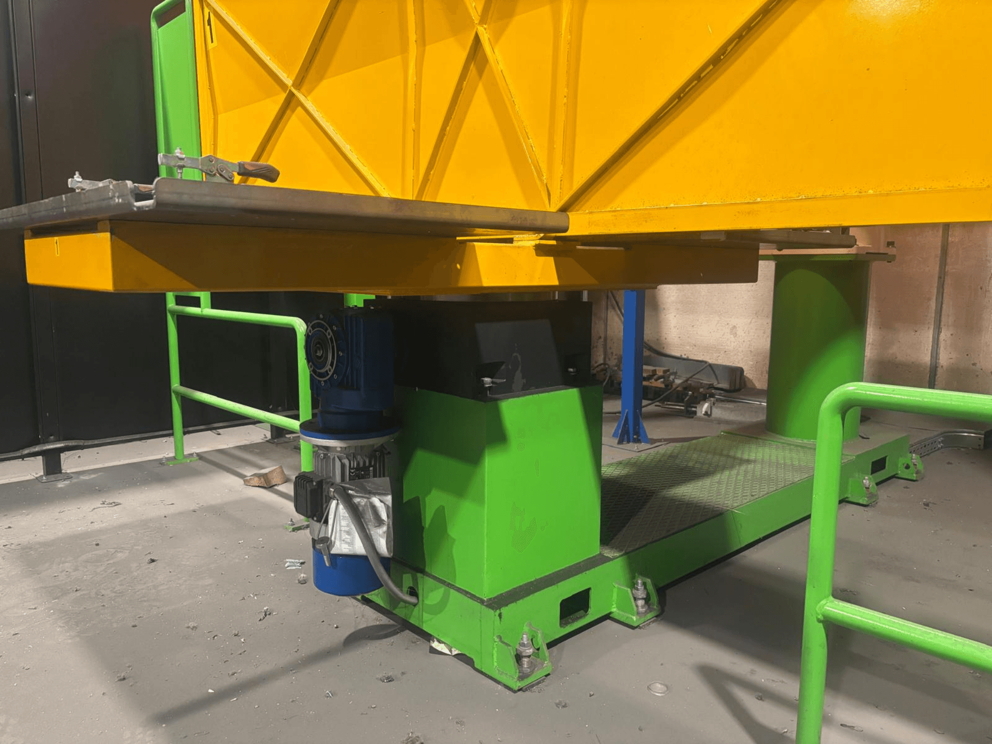 Grönt och gult industrimaskineri sett lågt framifrån, med motor och plattform med strukturerad yta.