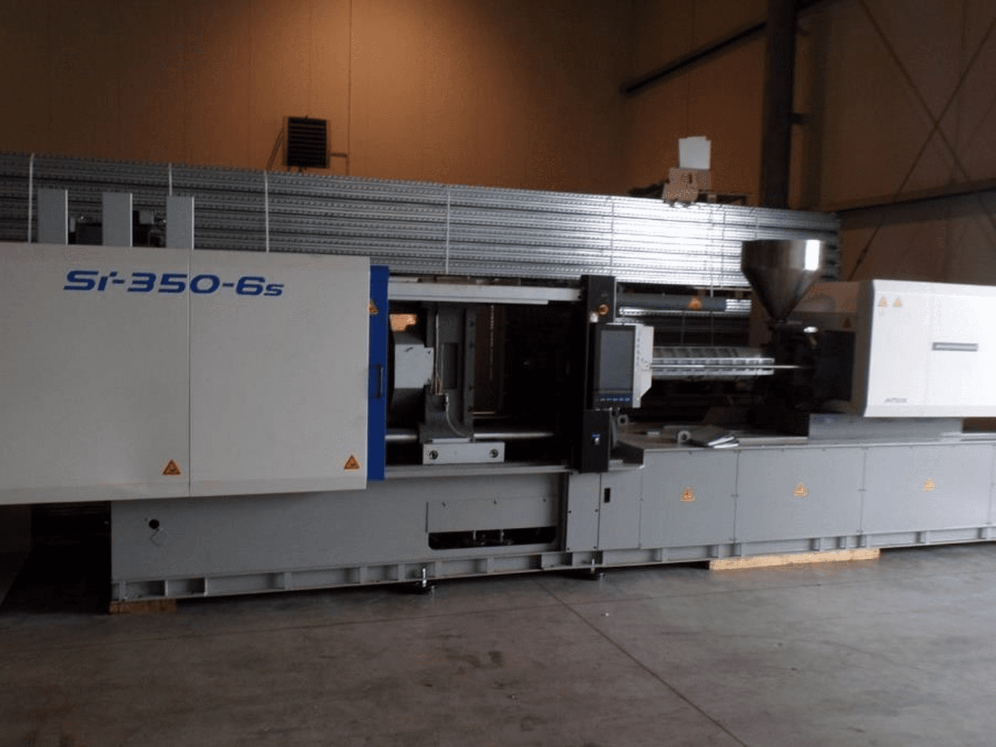 Si-350-6s formsprutningsmaskin i sidovy, med en behållare och kontrollpanel, placerad i en rymlig industrimiljö.