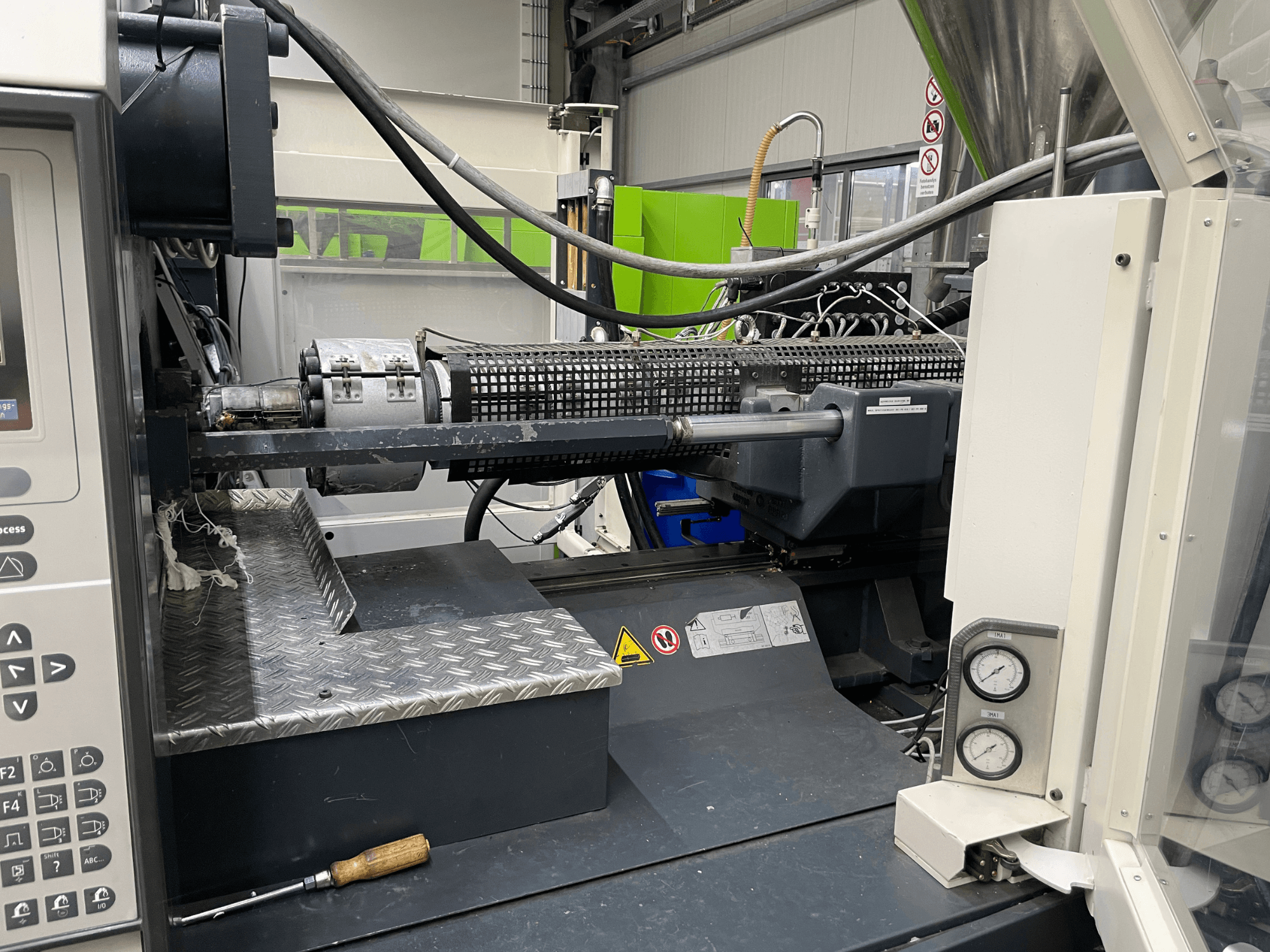 Formsprutningsmaskin i sidovy med kontrollpanel, extruder och tryckmätare synliga, perfekt för tillverkningsuppgifter.