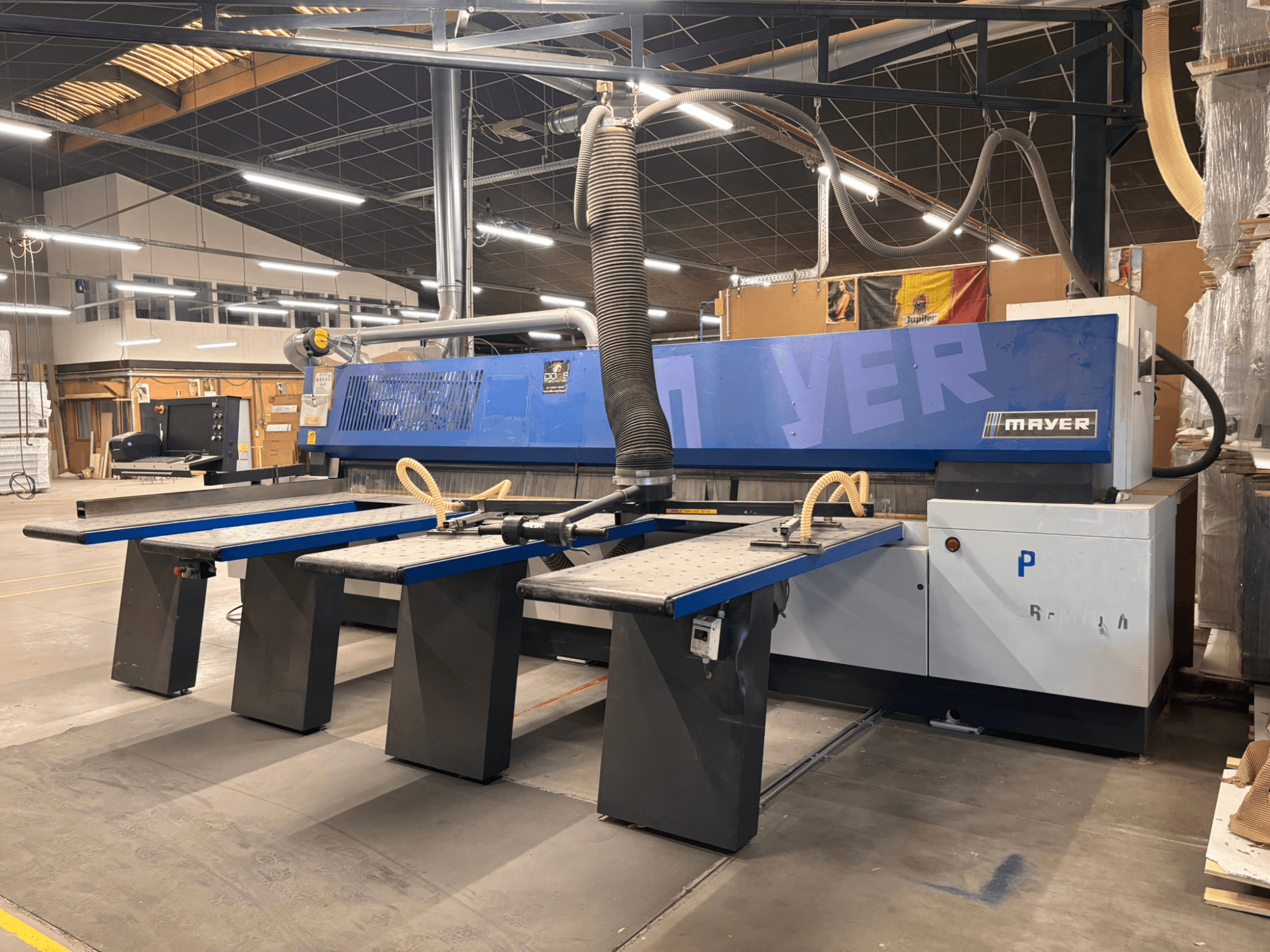 Mayer CNC-maskin med blå paneler, framifrån; har flera arbetsbord och ett dammutsugningssystem för träbearbetning.