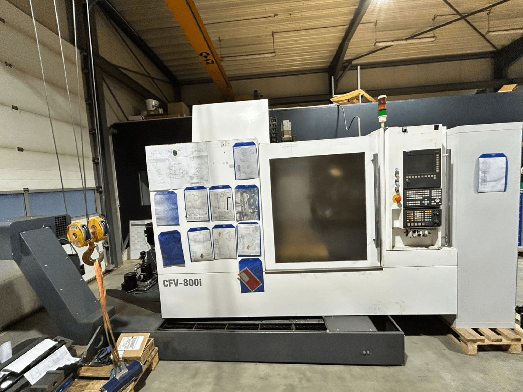 CFV-800i CNC-maskin visad framifrån, med kontrollpanel, dokument på sidan och traverskran i fabriksmiljö.
