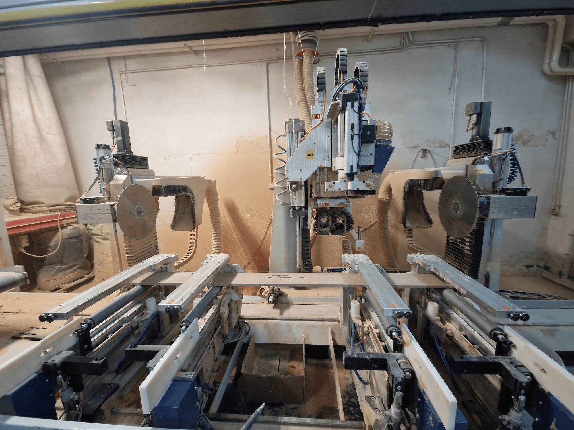 CNC-maskin med dubbla sågblad och skenor, sedd framifrån. Dammutsugningssystem synliga, lämpliga för träbearbetning.
