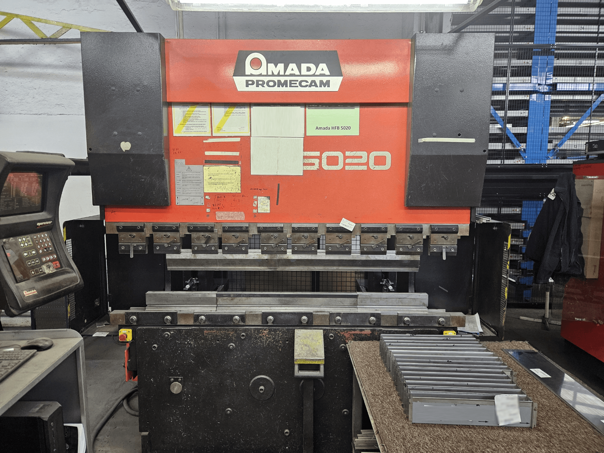 Amada HFBO 5020 kantpress framifrån, med kontrollpanel och staplade metalldelar på arbetsytan.
