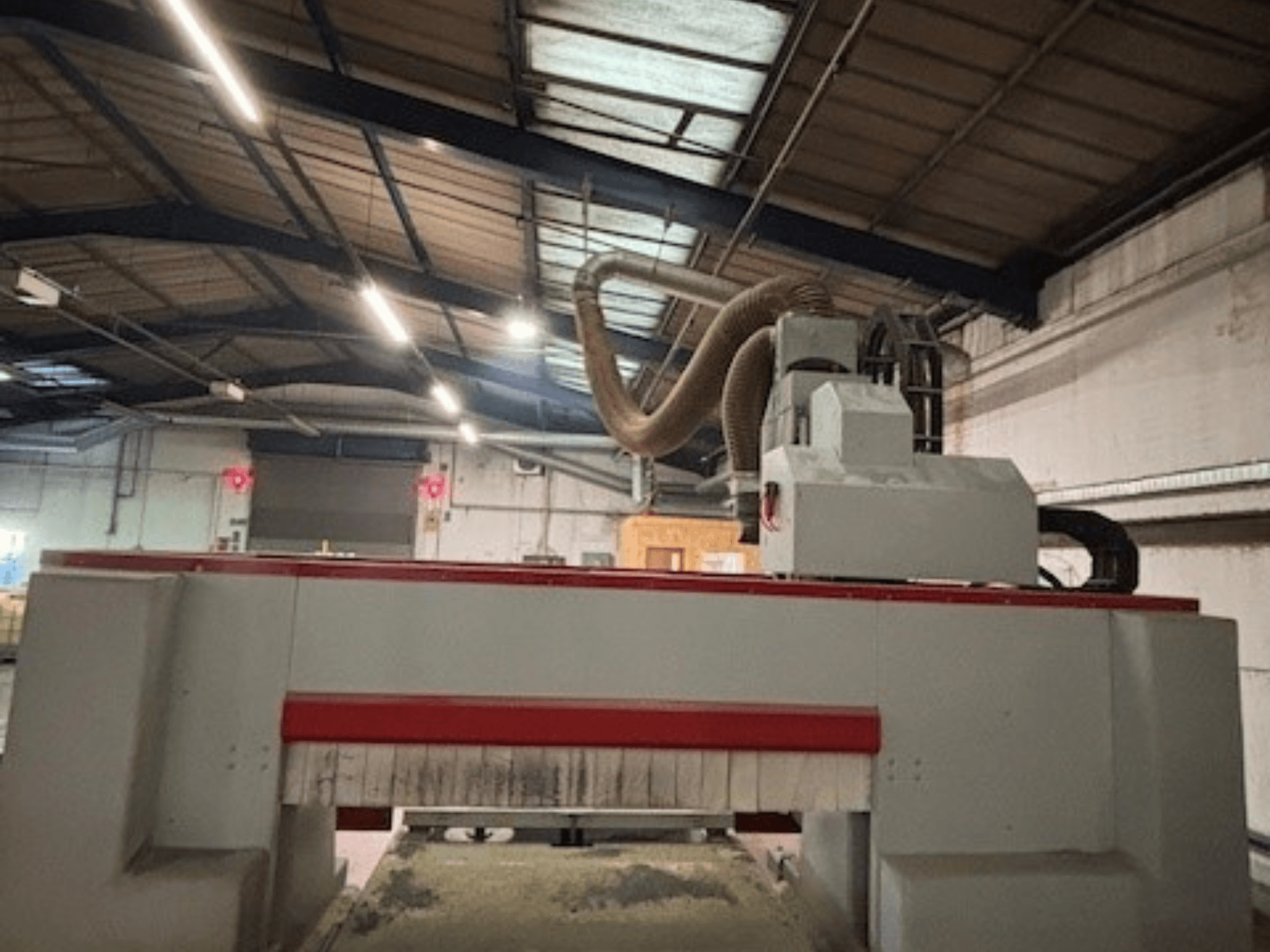 CNC-fräsmaskin i en verkstad, sidovy som framhäver den röda och grå designen, dammutsugningssystem monterat.