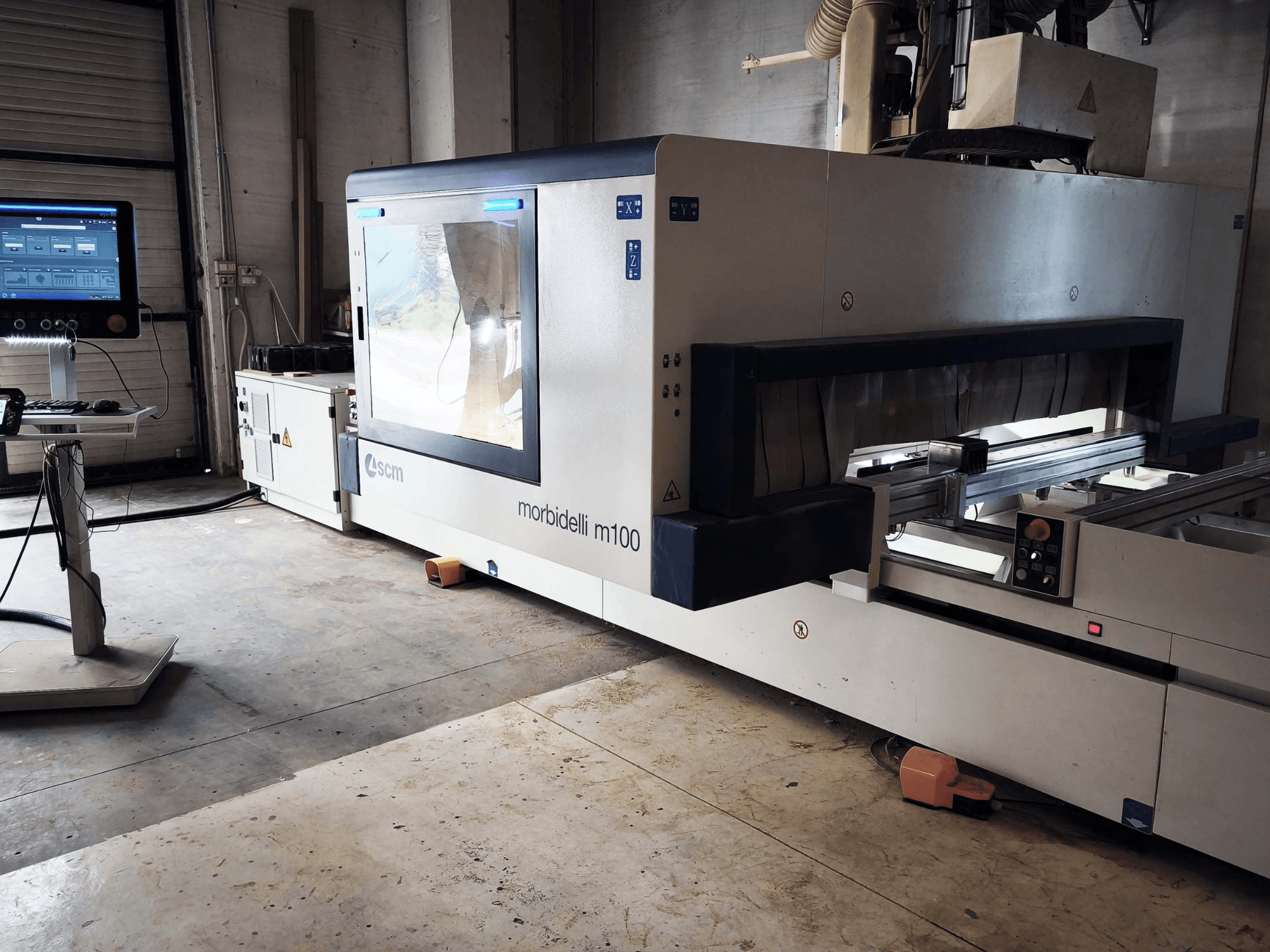 SCM Morbidelli M 100 CNC-bearbetningscenter för trä i sidovy, där kontrollpanelen, arbetsområdet och säkerhetsfunktionerna visas.