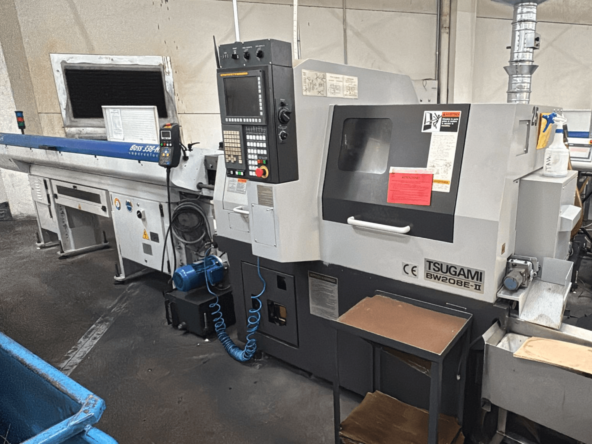 Tsugami BW208E-II CNC-maskin i en verkstad, sedd framifrån, med kontrollpanel och säkerhetsetiketter synliga.