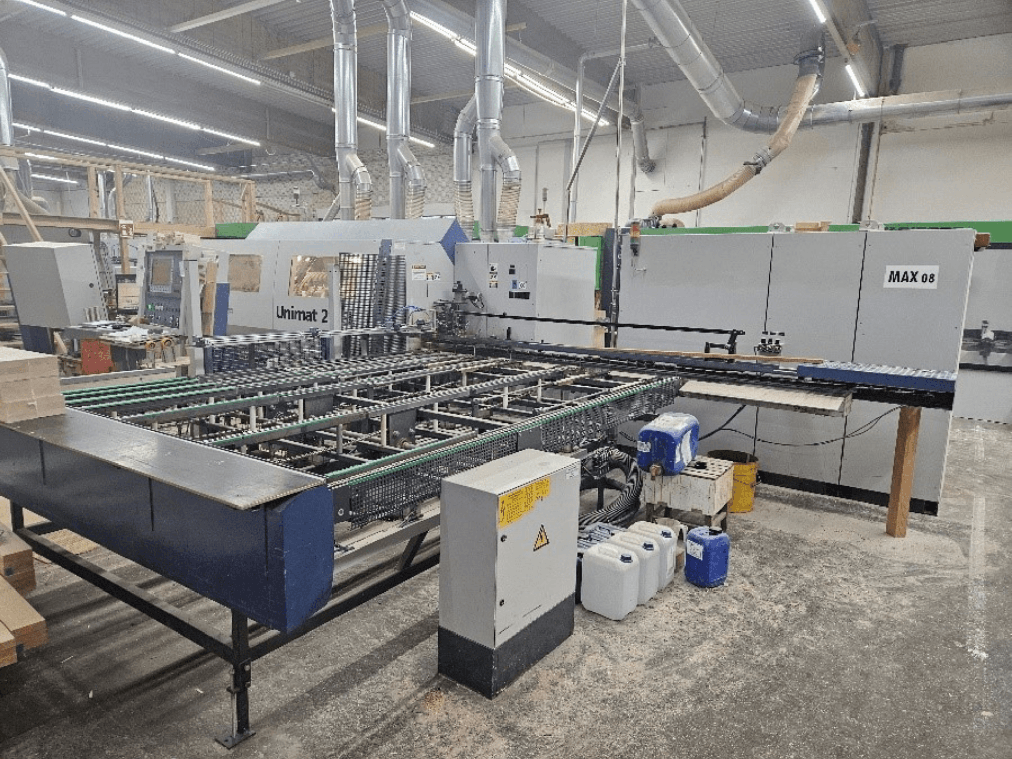 Sidovy av en Unimat 2 CNC-maskin i en verkstad, med transportband och tekniska komponenter med synlig Max 08-enhet.