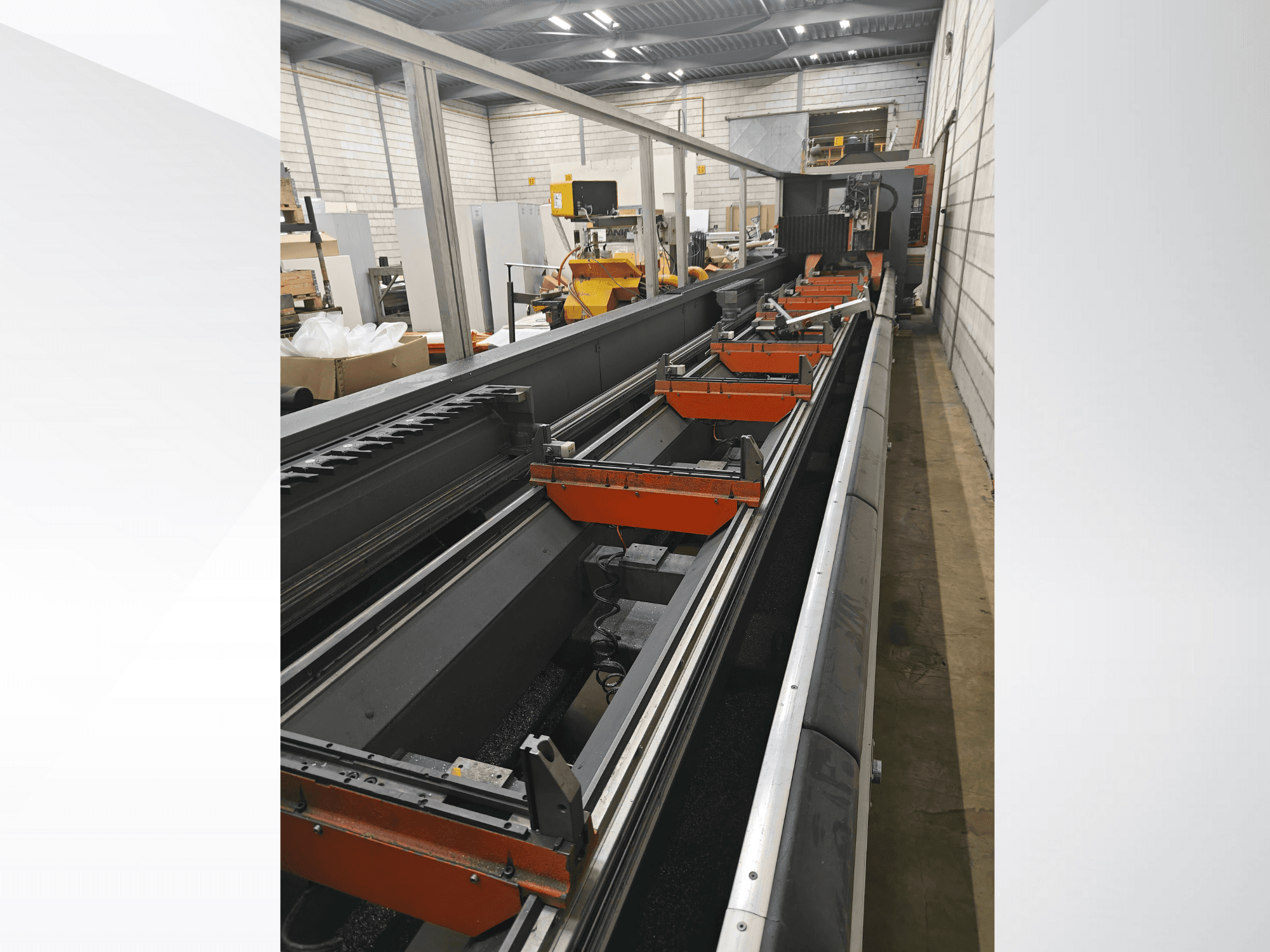 Industriell CNC-maskin i sidovy med linjära skenor, orangefärgade klämmor och precisionskomponenter i en lagerlokal.