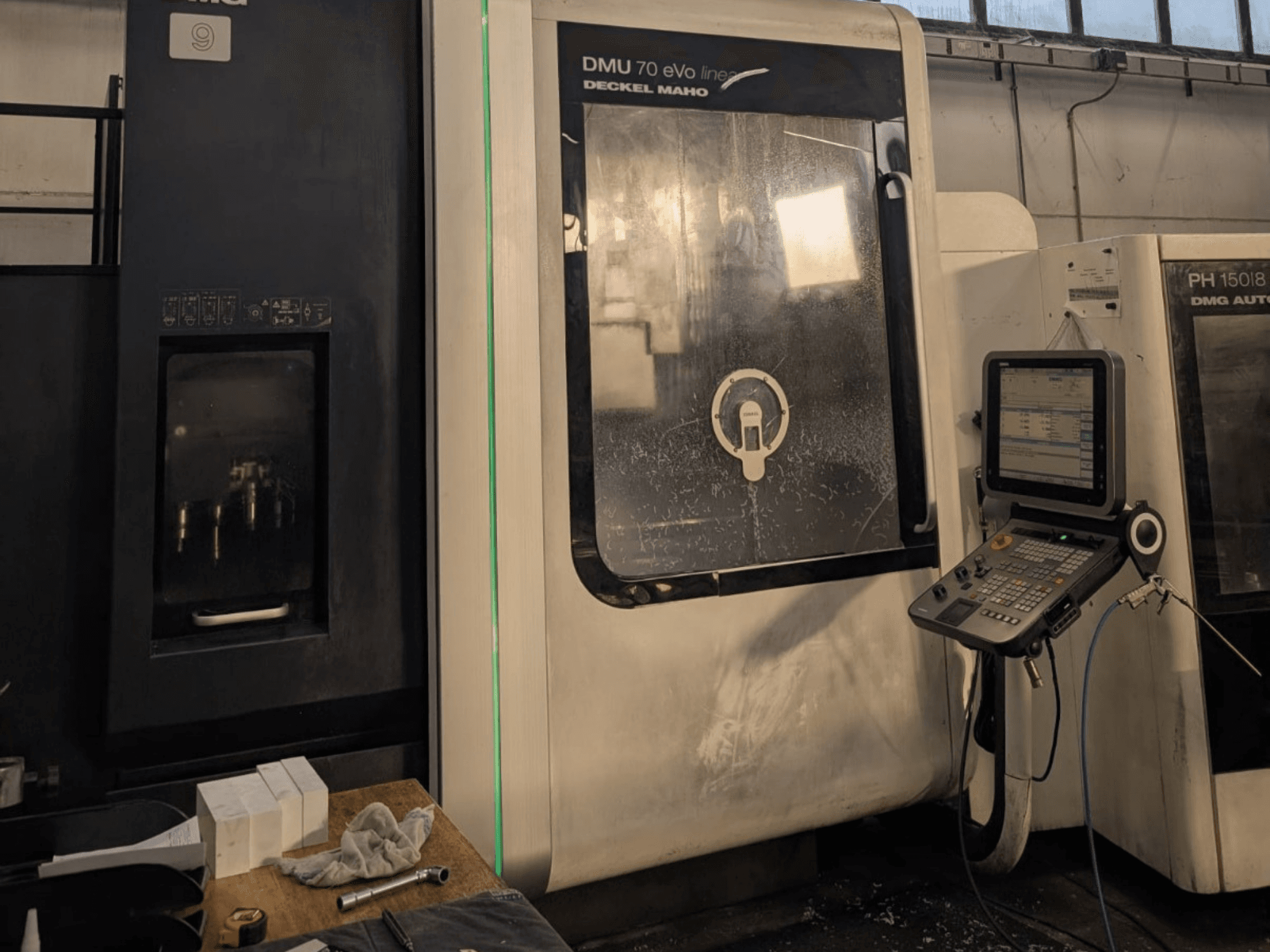 DMG DECKEL MAHO DMU 70 EVO Linjär vertikal bearbetningscenter, framifrån med kontrollpanel, verktyg och arbetsyta synliga.