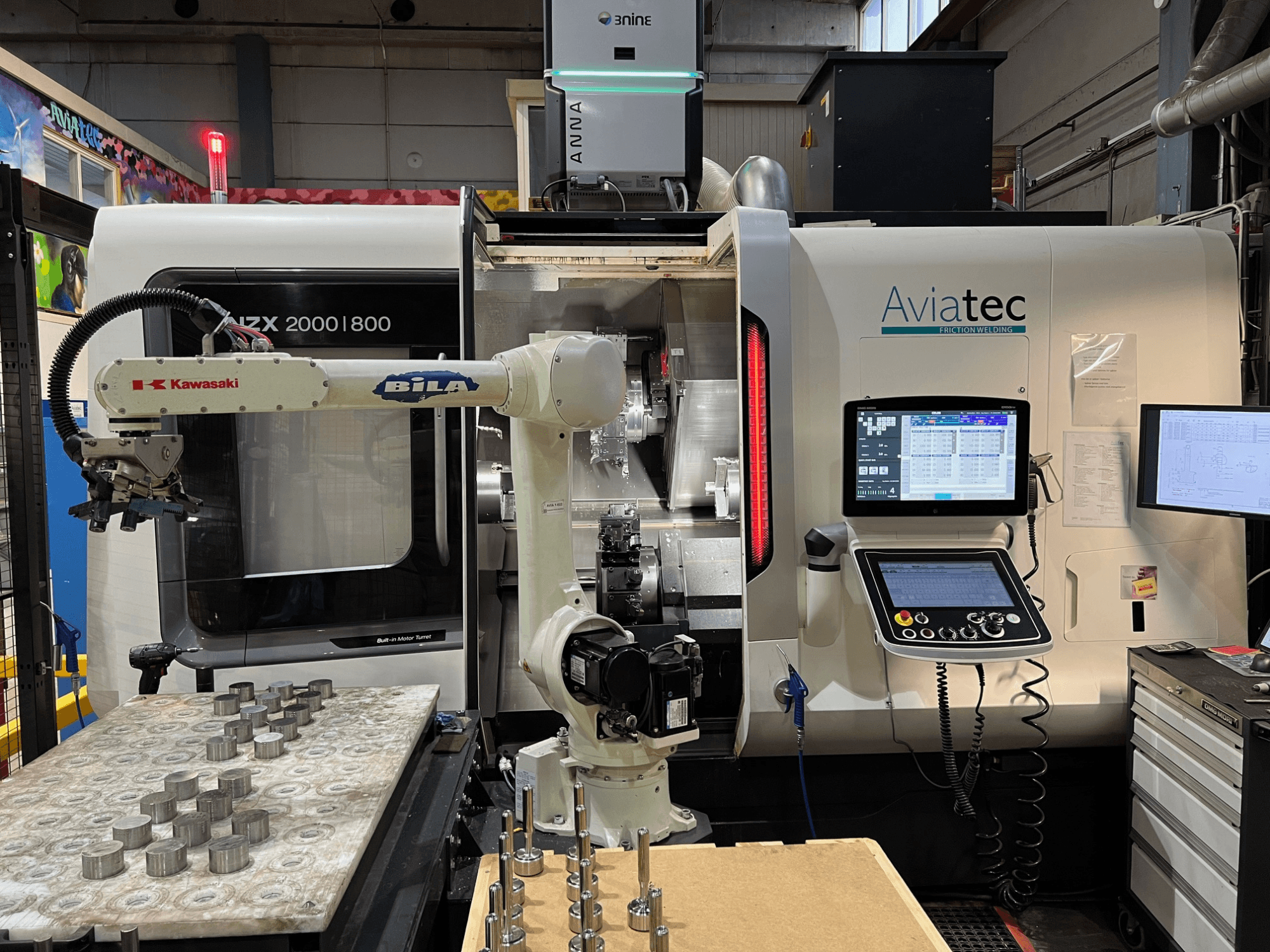Horisontell svarv DMG MORI NZX 2000/800SY med Kawasaki-robotarm, kontrollpanel och metallkomponenter på arbetsbordet.