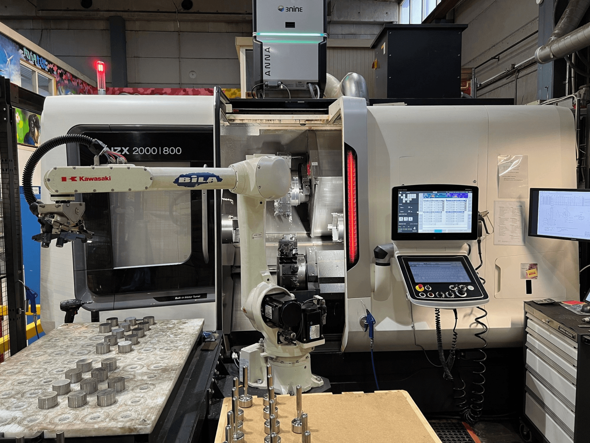 En horisontell svarv av typen DMG MORI NZX 2000/800SY i en verkstad, där Kawasakis robotarm och styrsystem syns.