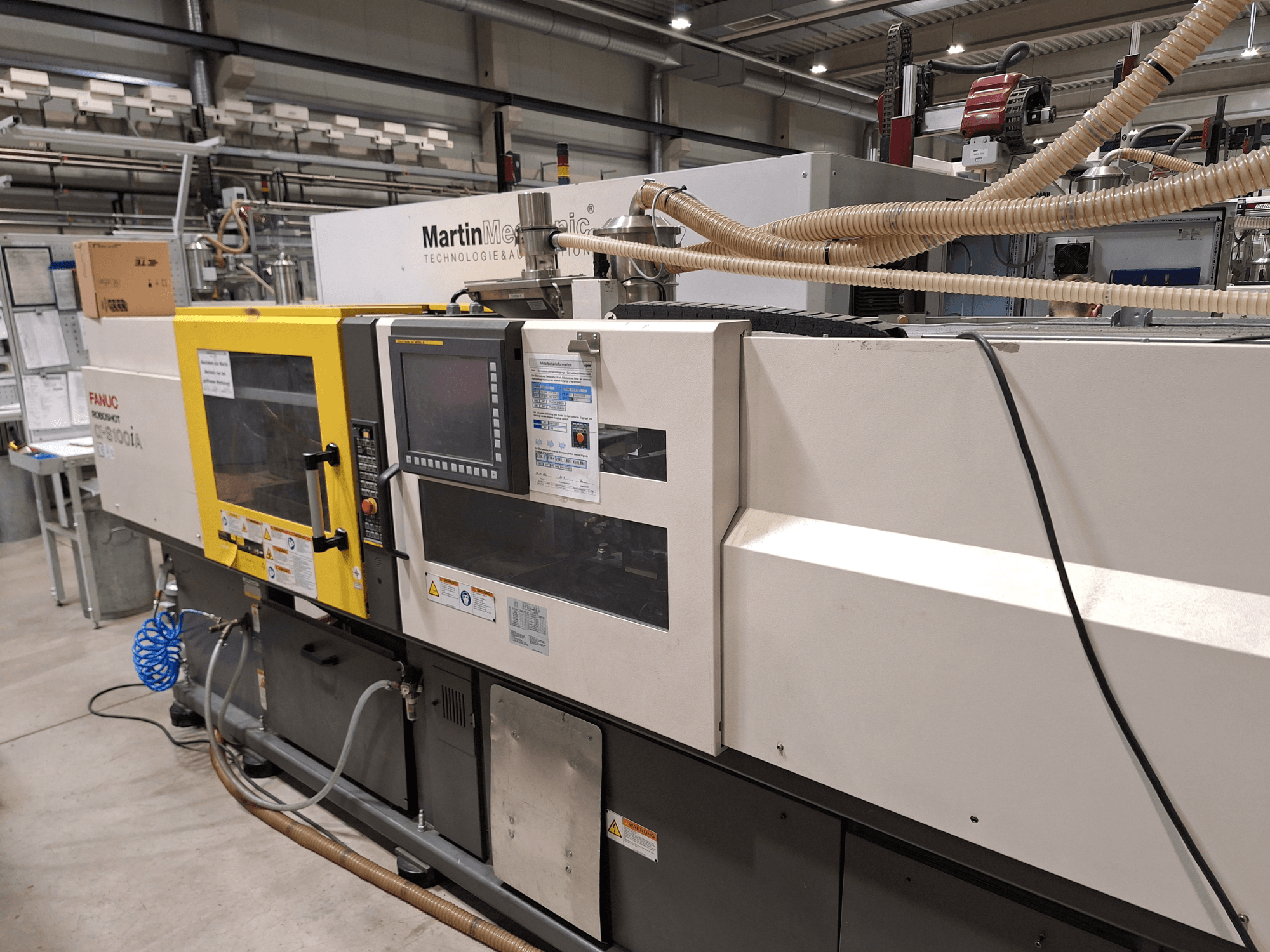 FANUC Roboshot S100iA elektrisk formsprutningsmaskin, sidovy, utrustad med pekskärm och säkerhetsetiketter.