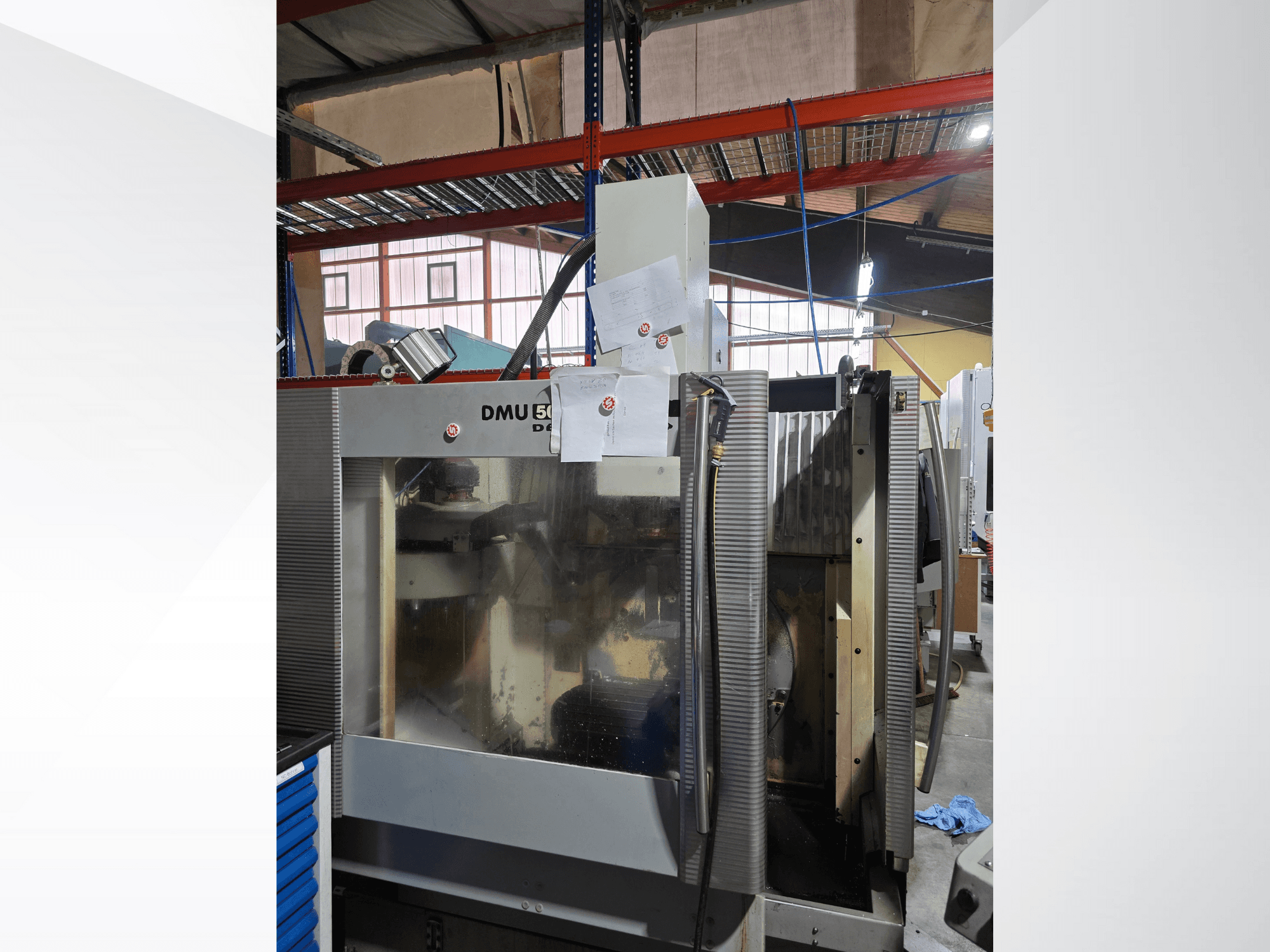 DMU 50 3-axlig CNC-bearbetningscenter i en verkstad, sett framifrån, med driftskomponenter och bifogade dokument.