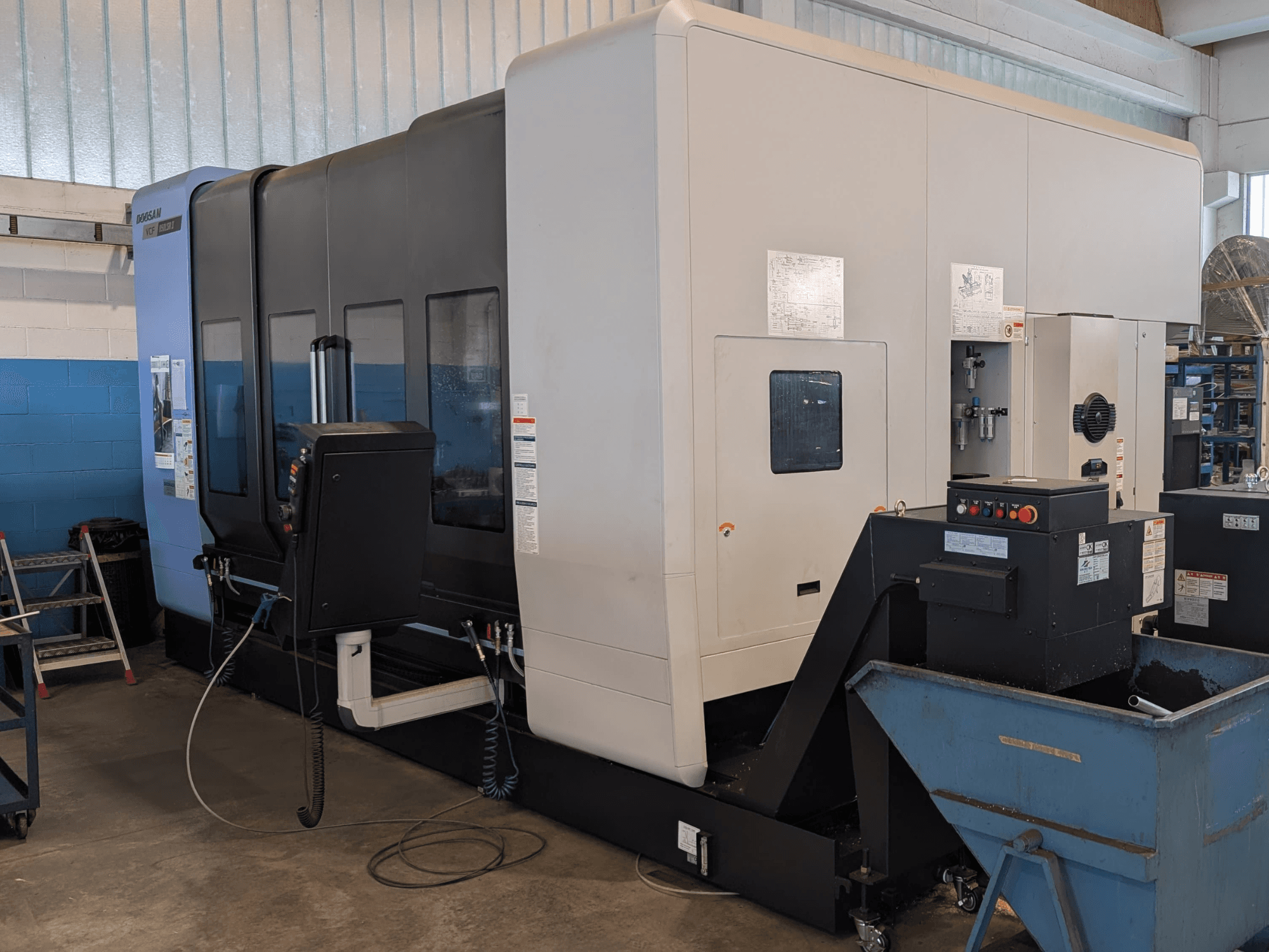 Vertikalt bearbetningscenter DOOSAN VCF850LSR-II sett från sidan, där man kan se kontrollpanelen, kylmedelssystemet och den robusta konstruktionen.