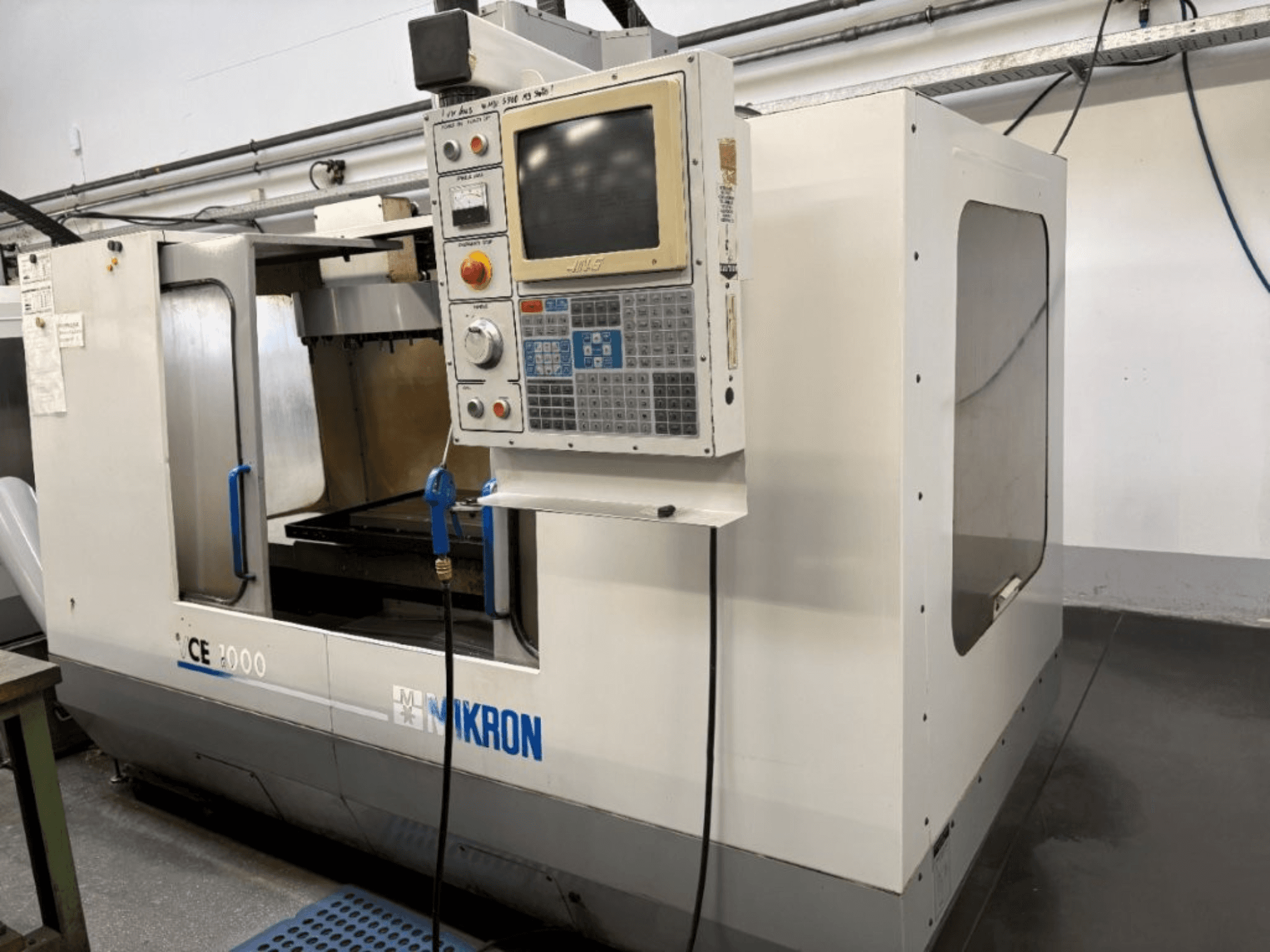 Mikron CE 2000 CNC-maskin, vy framifrån; har en kontrollpanel med knappar och skärm, silverfärgad utsida och arbetsområde.