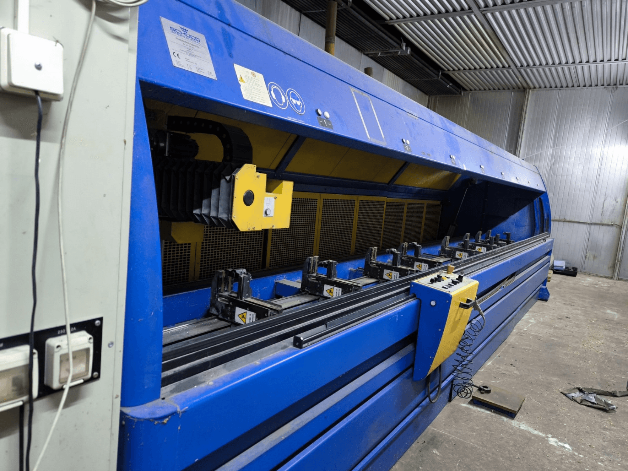 Schneider industriell skärmaskin i blått, vy från sidan, med kontrollpanel, remmar och flera fastspänningsstationer synliga.