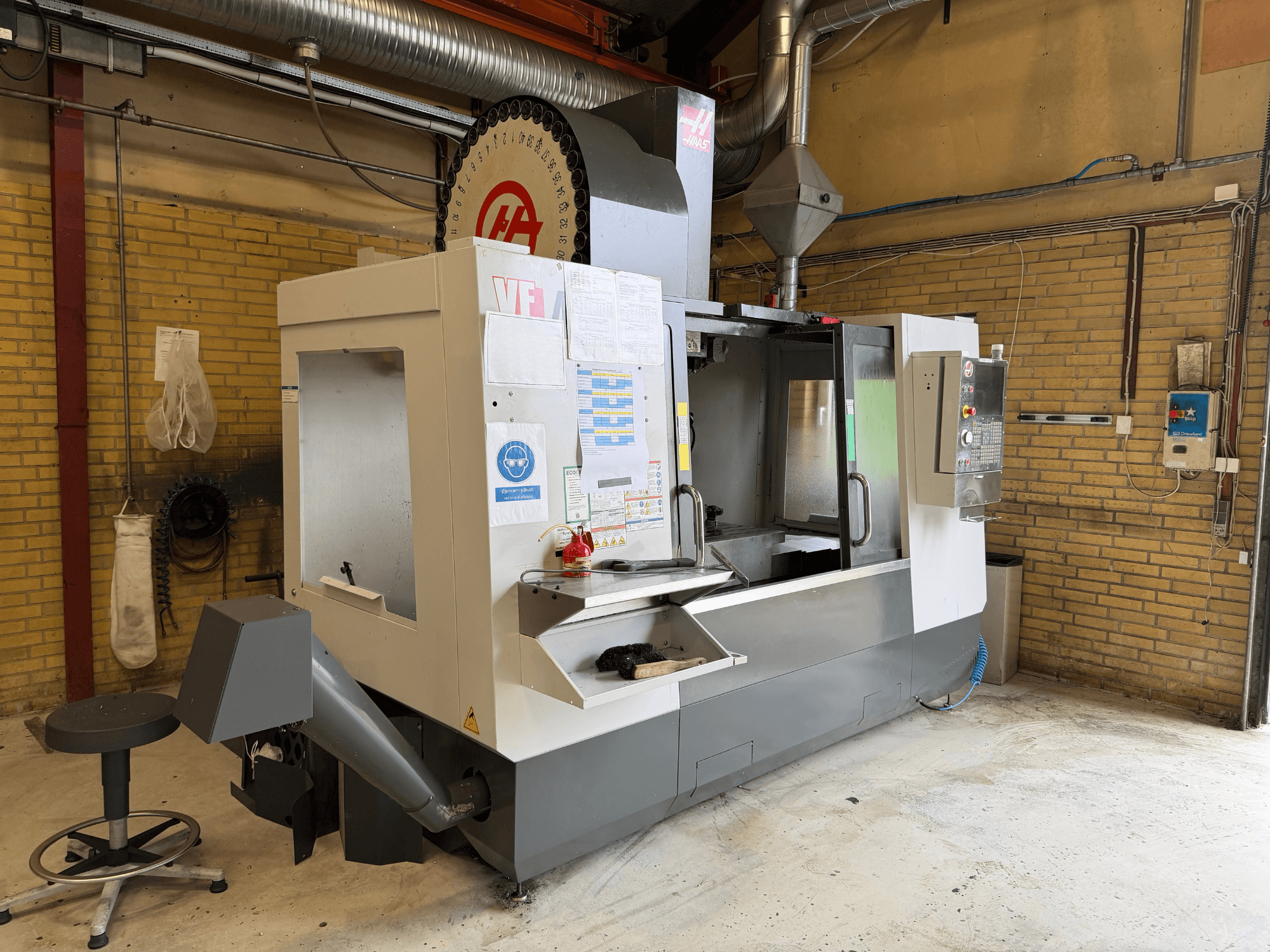 HAAS VF-4 vertikalt bearbetningscenter, framifrån; med kontrollpanel, verktygshållare och produktionsuppställning i bakgrunden.