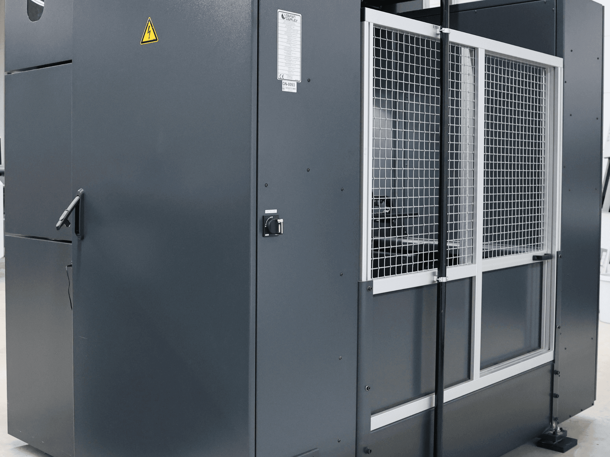 Grå industrimaskin med säkerhetsvarning, framifrån med nätdörr och kontrollpanel, modellmärkt.
