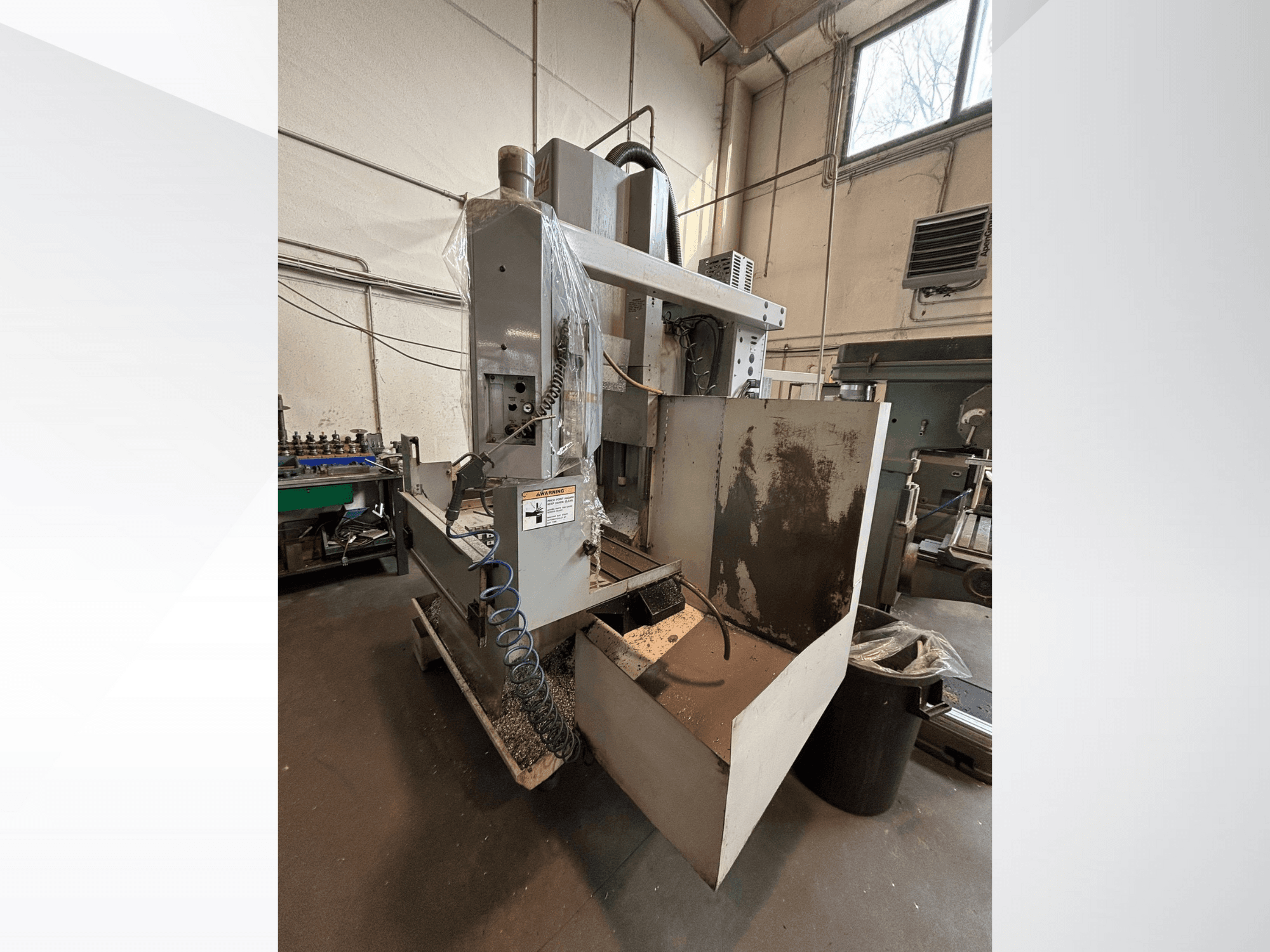 Vertikal fräsmaskin med skyddskåpa, sidovy; inkluderar kylvätskeslang och kontrollpanel synlig. Idealisk för maskinbearbetning.