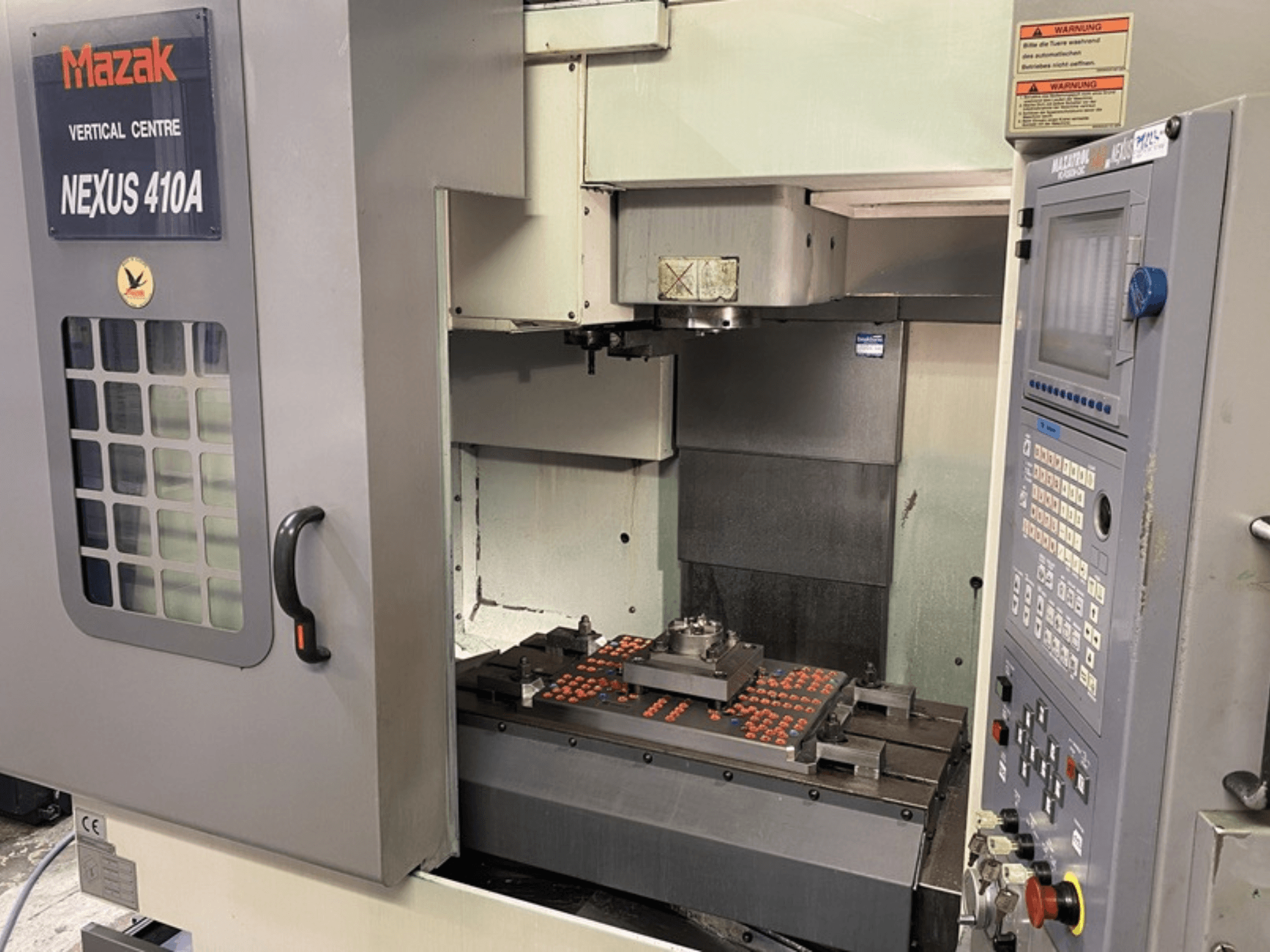 Mazak NEXUS 410A vertikal fleroperationsmaskin, framifrån, med synlig kontrollpanel och verktygsmaskinsuppställning på arbetsytan.