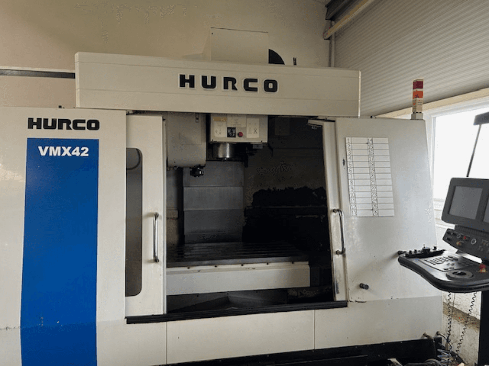 Hurco VMX42 CNC-maskin framifrån, med kontrollpanel, spindel och arbetsområde; avslöjar driftlayout.